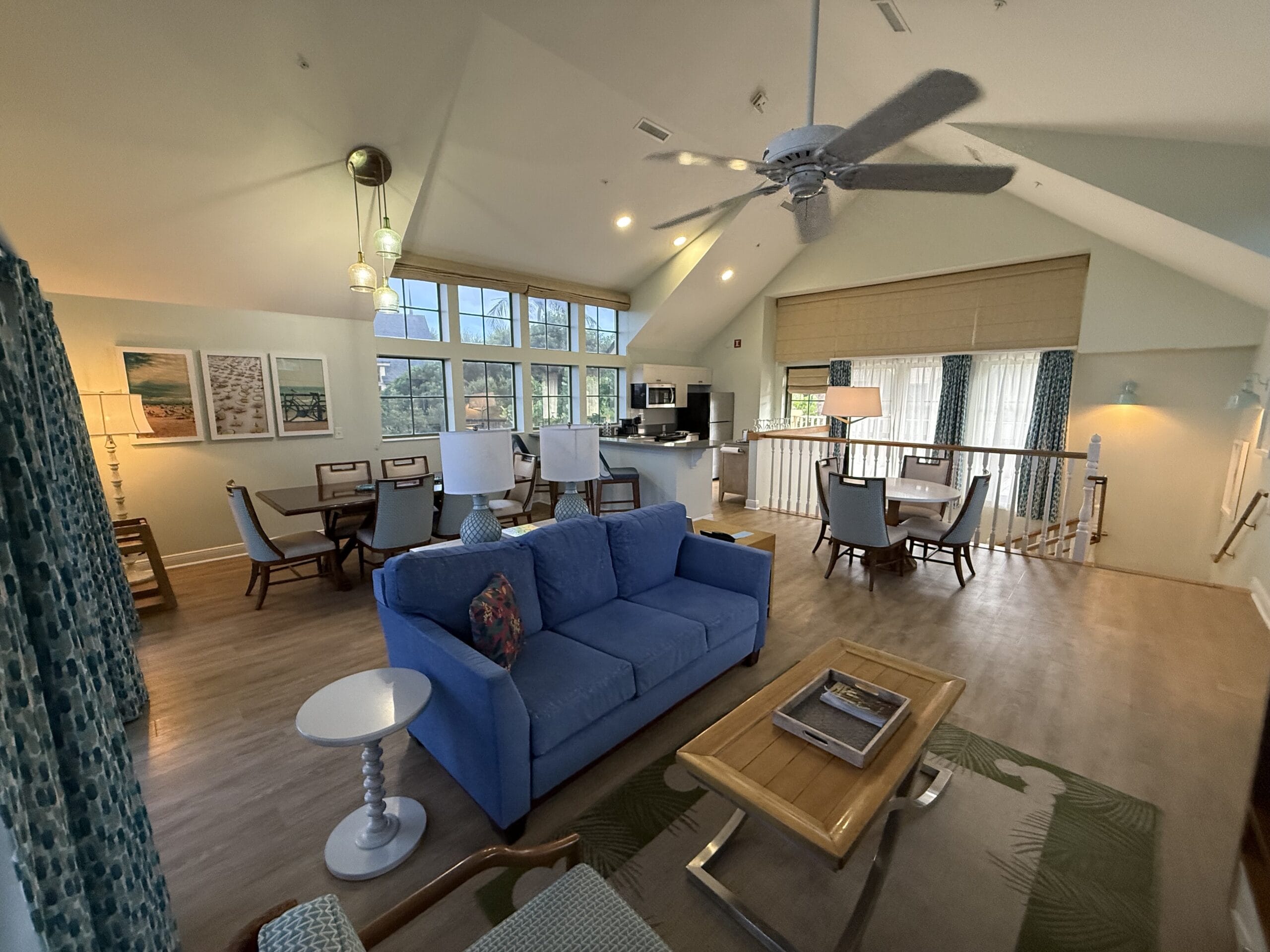 Spacious, sunlit living room at Disney’s Vero Beach Resort, blue sofa, dining tables, large windows with treetop views—no castle here!