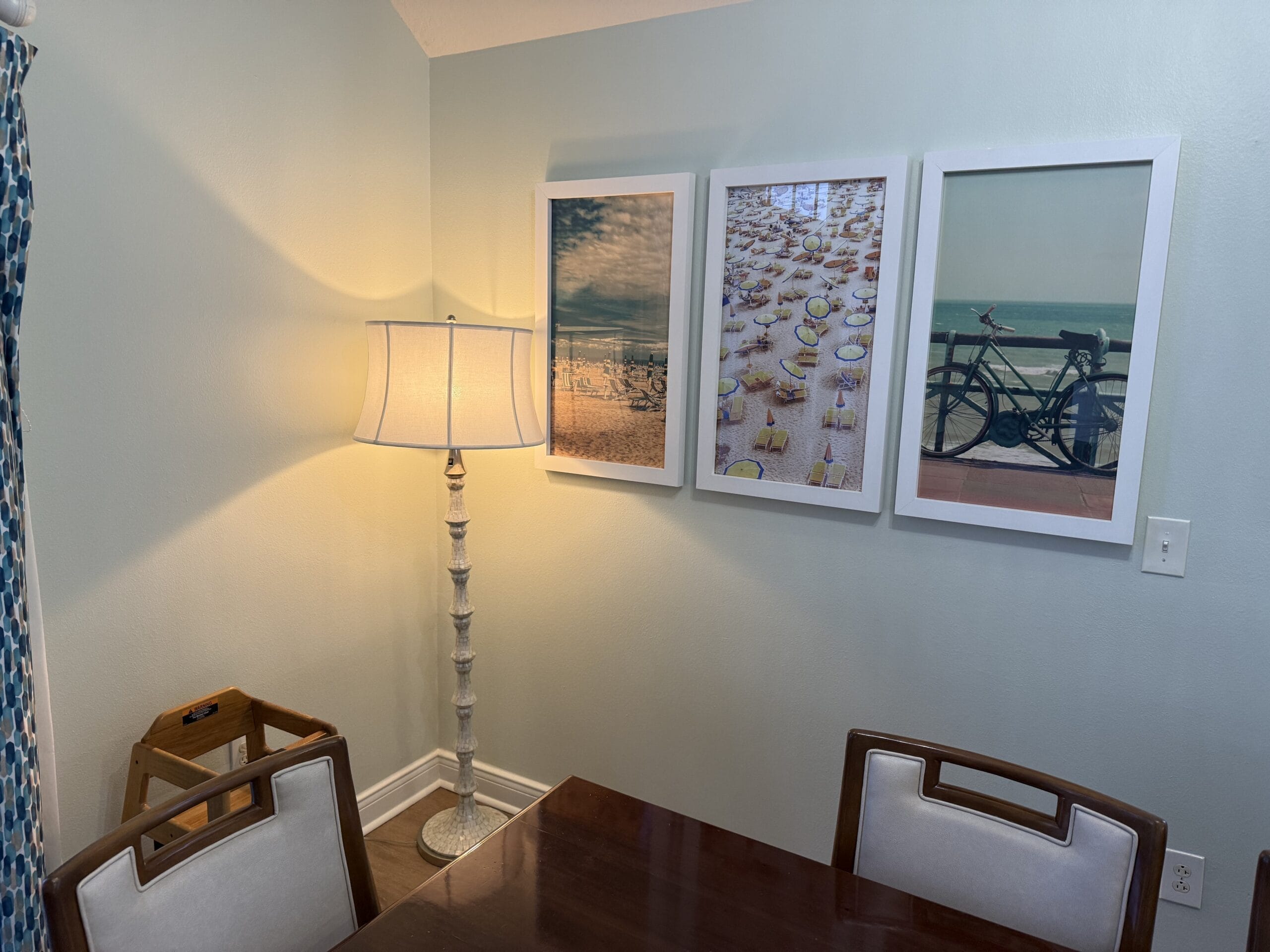 A cozy dining room corner at Disney's Vero Beach Resort 3 Bedroom Cottage with wooden table, floor lamp, and beach-themed wall art.