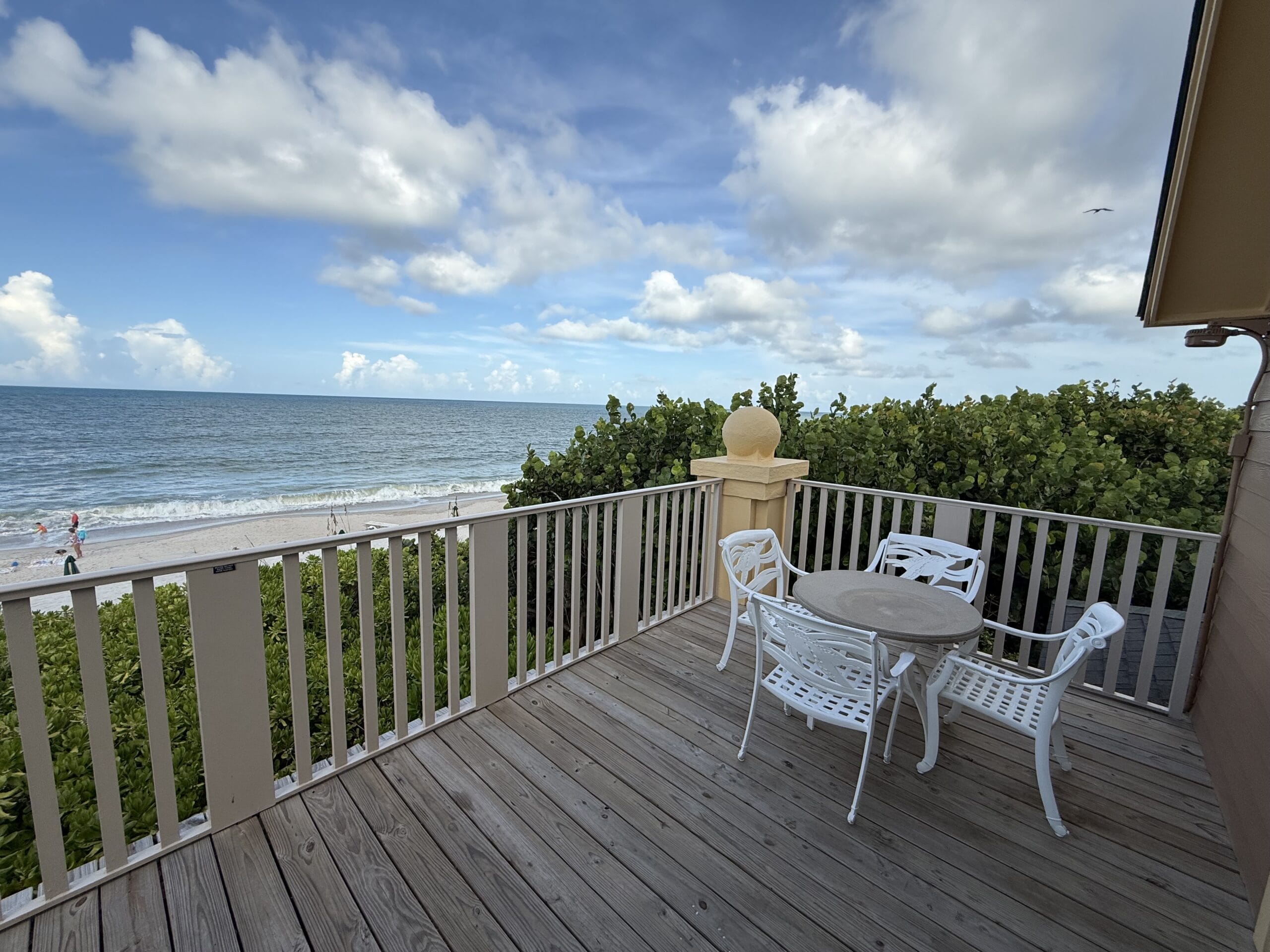 A wooden balcony with white patio furniture at Disney's Vero Beach Resort 3 Bedroom Cottage overlooks the Atlantic Ocean.
