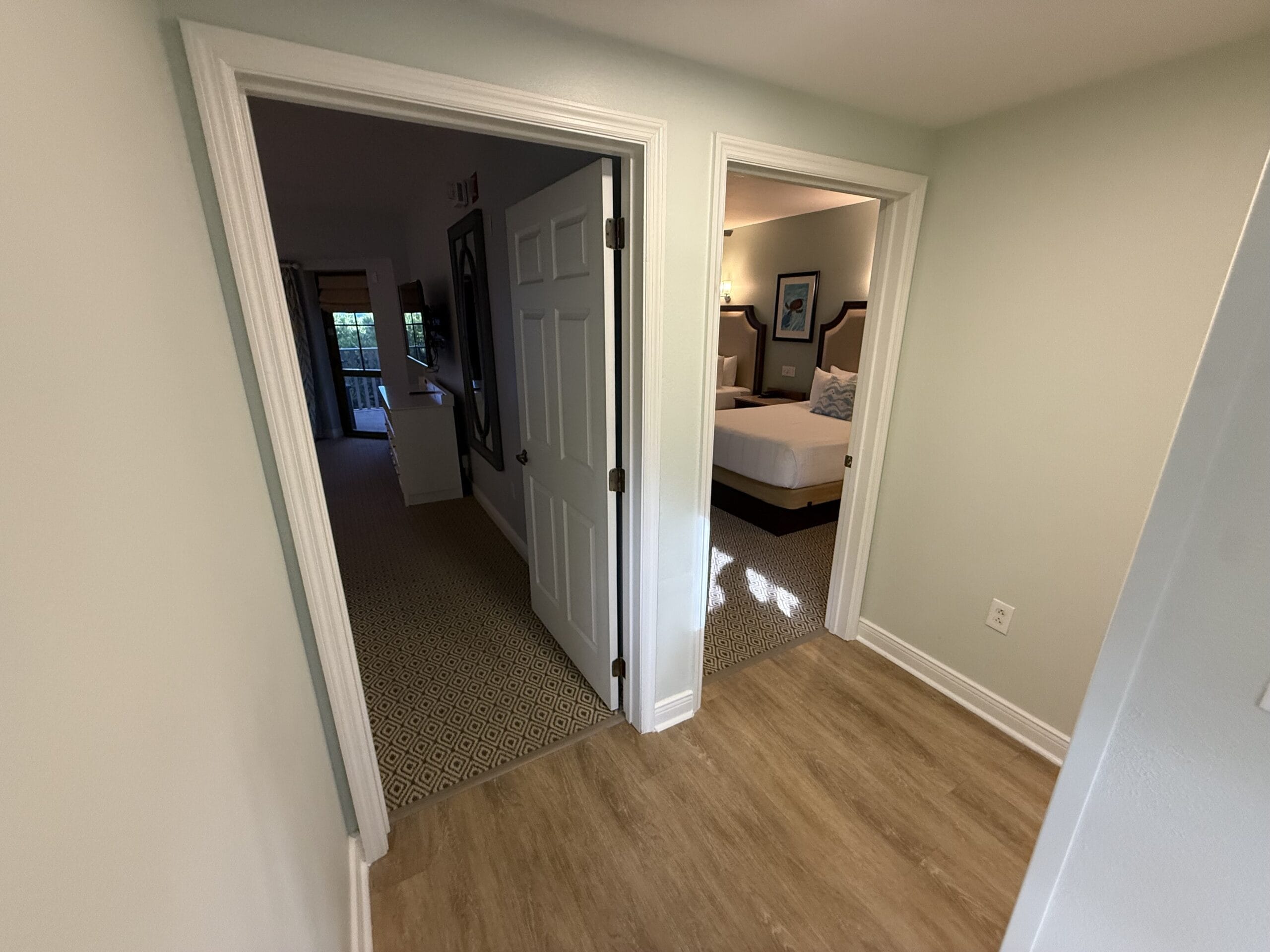 Two open doors in Disney’s Vero Beach Resort cottage, leading to a cozy bedroom and a bright, carpeted hallway—no castle views.