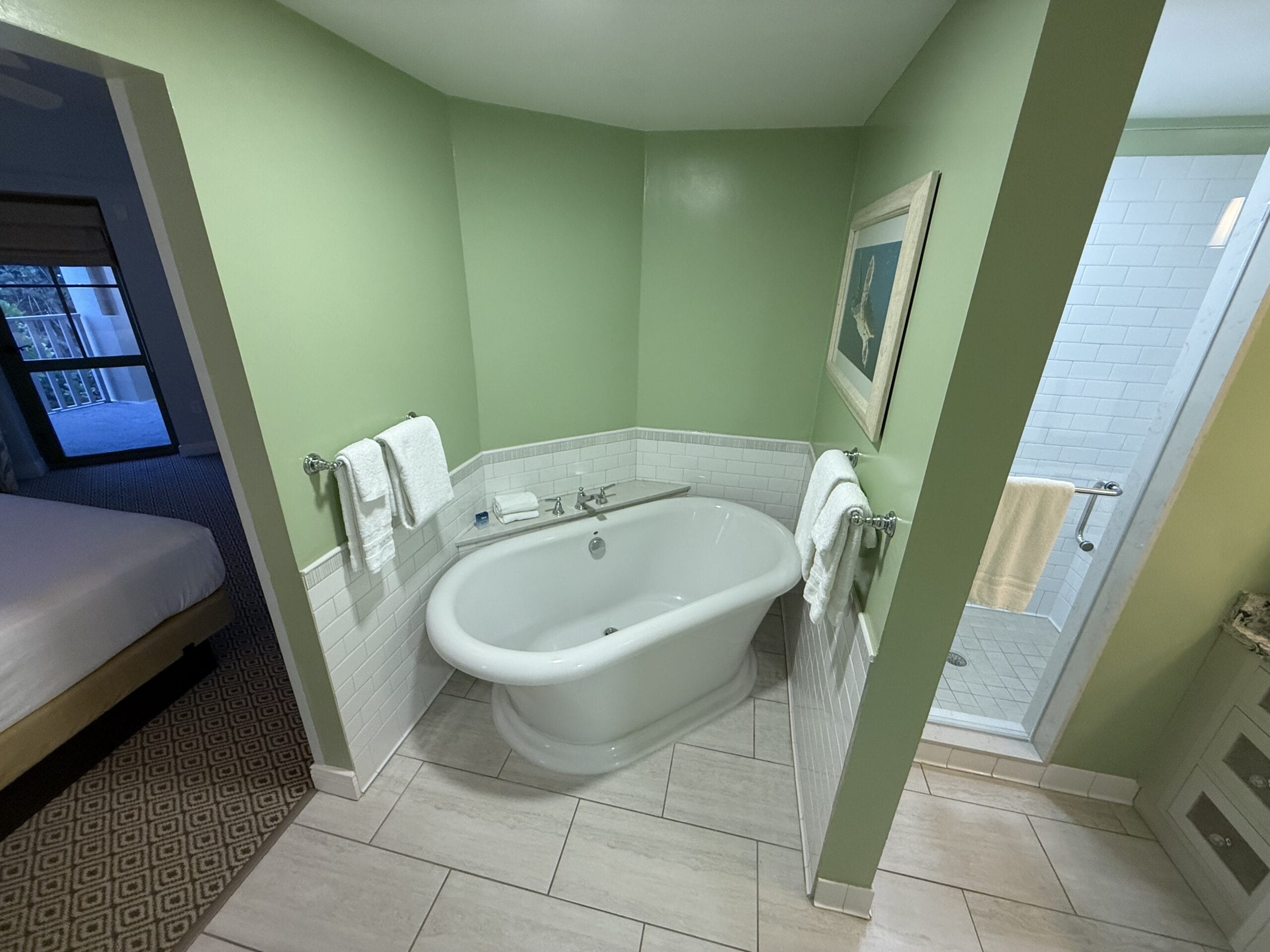 A white bathtub in a green bathroom at Disney's Vero Beach Resort, towels on rails, with a shower and bedroom nearby—no castle views.