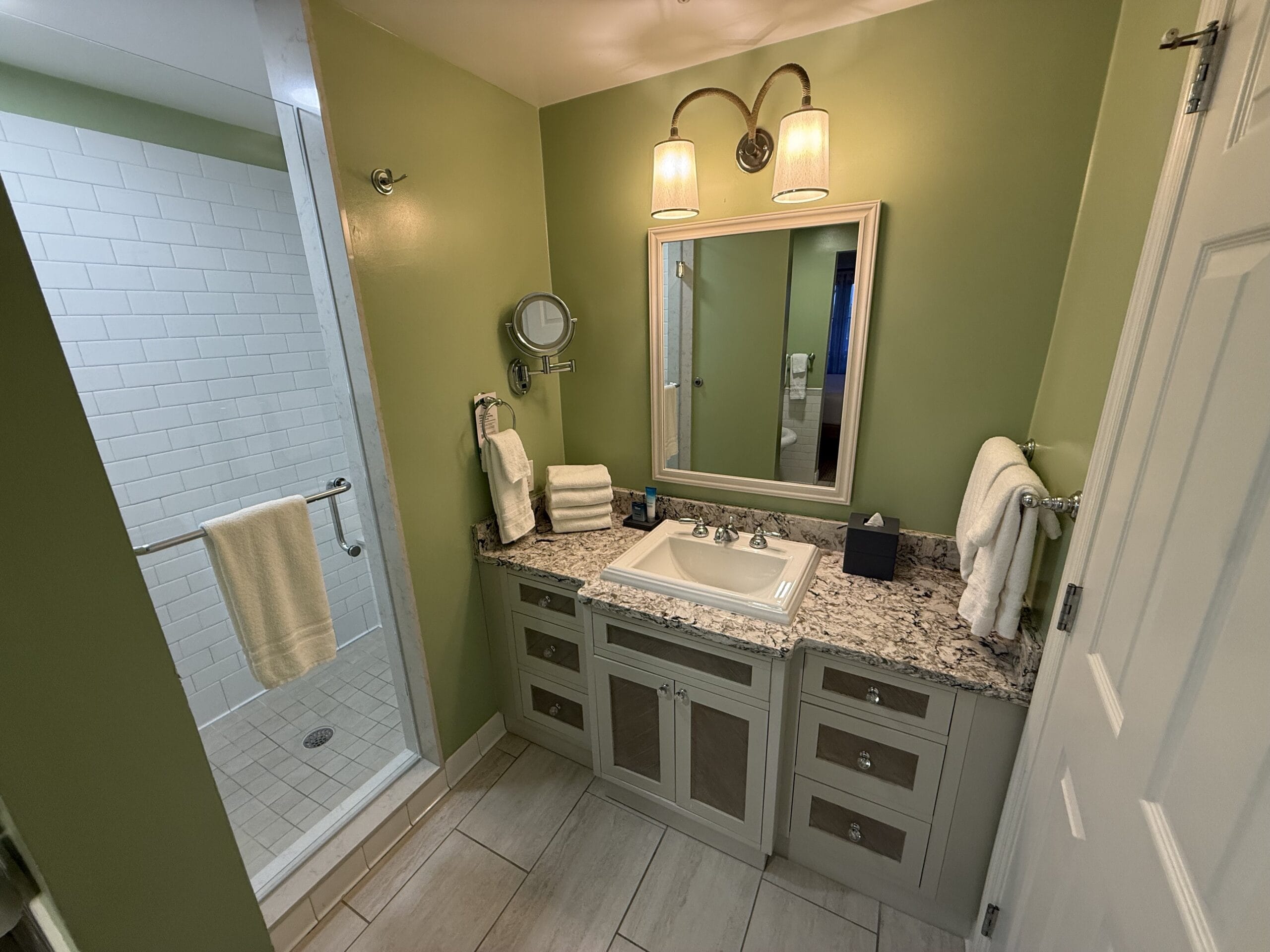 A cozy bathroom at Disney's Vero Beach Resort Cottage has green walls, a shower, vanity sink, and Disney-themed lighting touches.