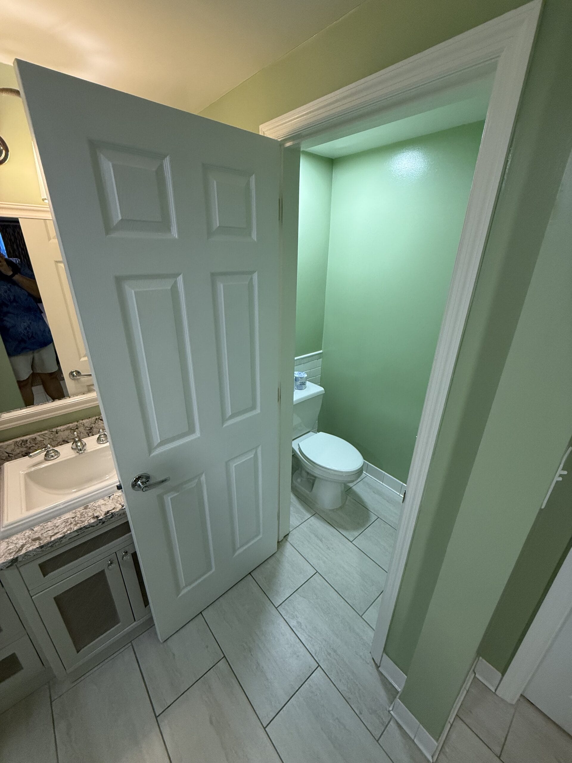 Bathroom at Disney's Vero Beach Resort, featuring a white door, mirror above sink, and green-walled toilet; not a castle scene.