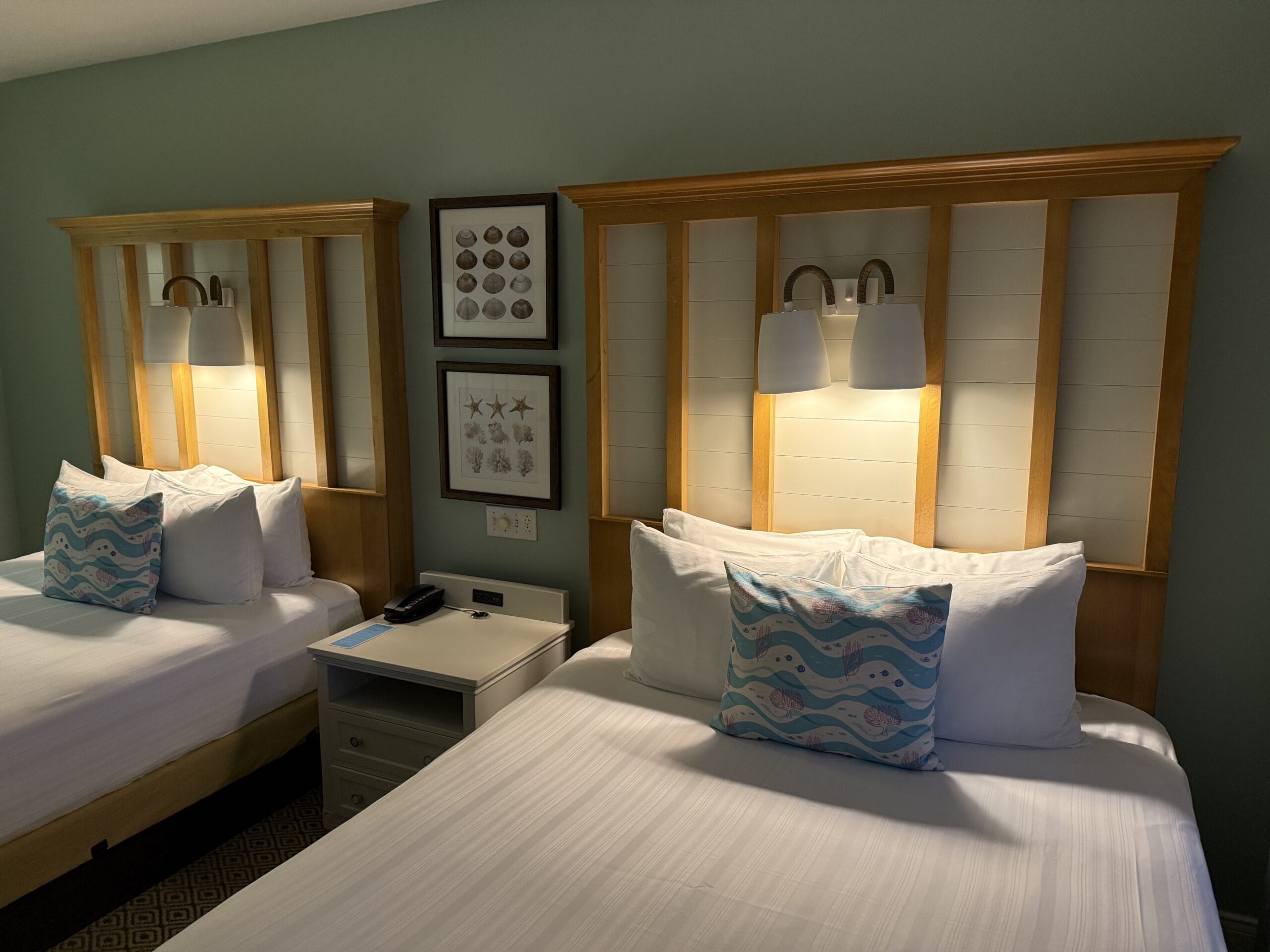 Two neatly made beds with patterned pillows and white linens in a cozy Disney's Vero Beach Resort cottage, no castle visible here.