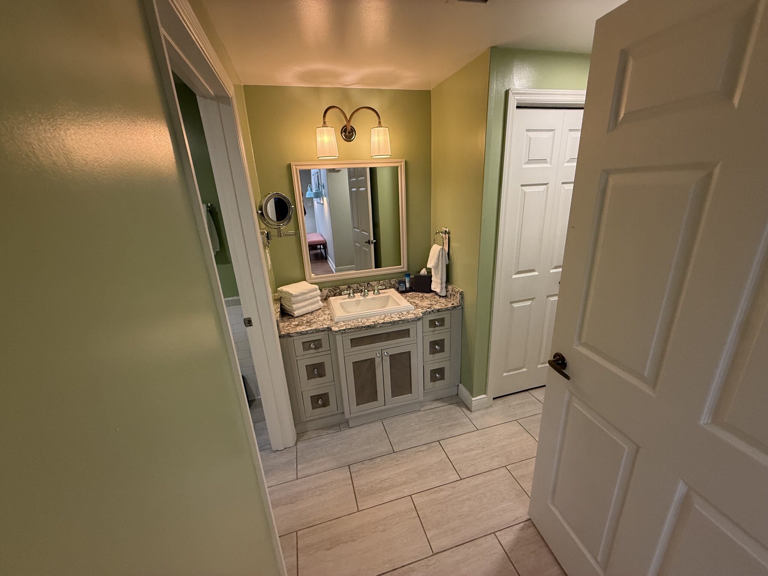 Bathroom with green walls, white vanity, and towels, capturing the cozy Disney Cottage vibe found at Disney’s Vero Beach Resort.