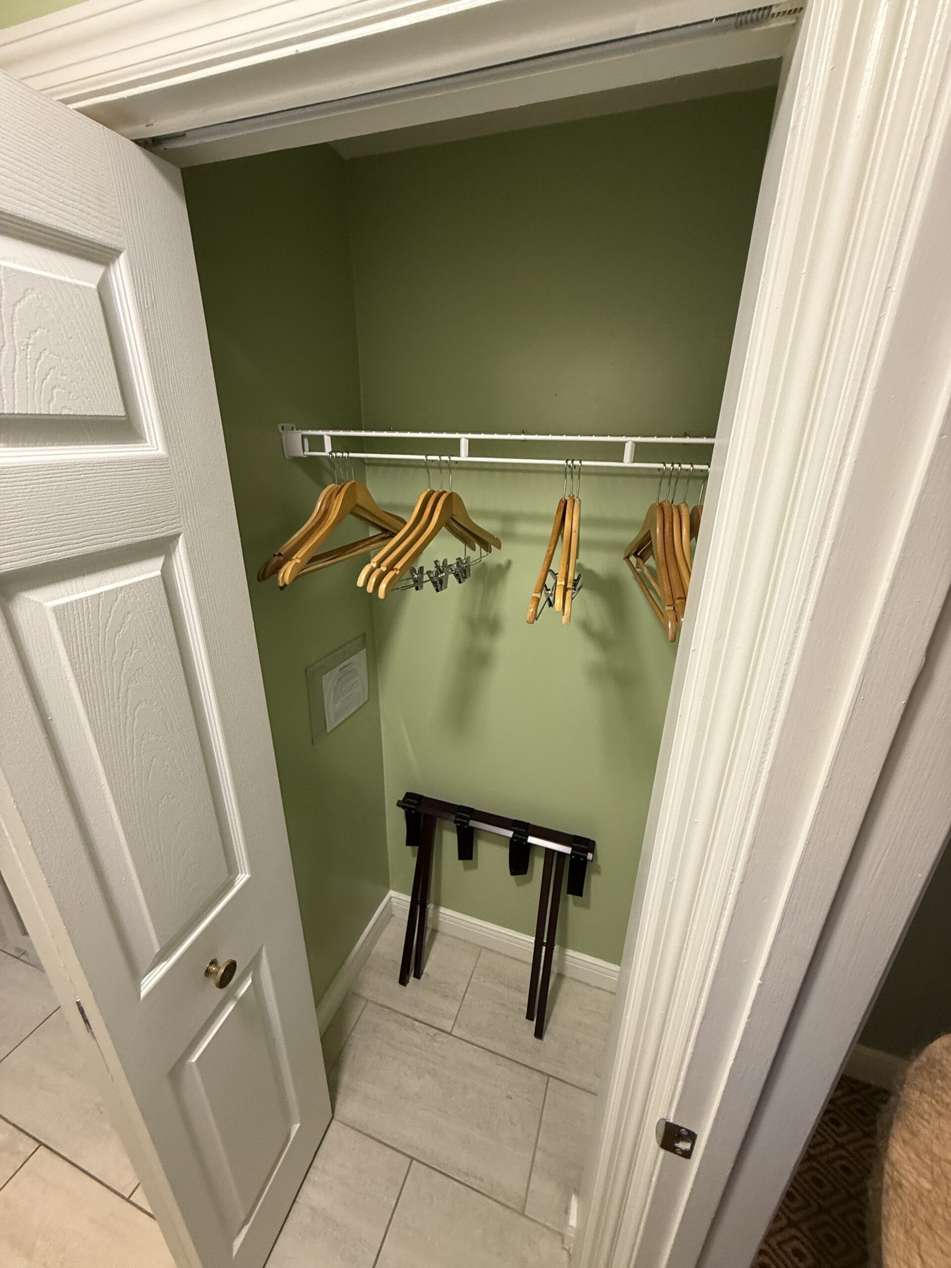 Small closet at Disney’s Vero Beach Resort Cottage with green walls, wire shelf with hangers, and a folded luggage rack—no castle here.