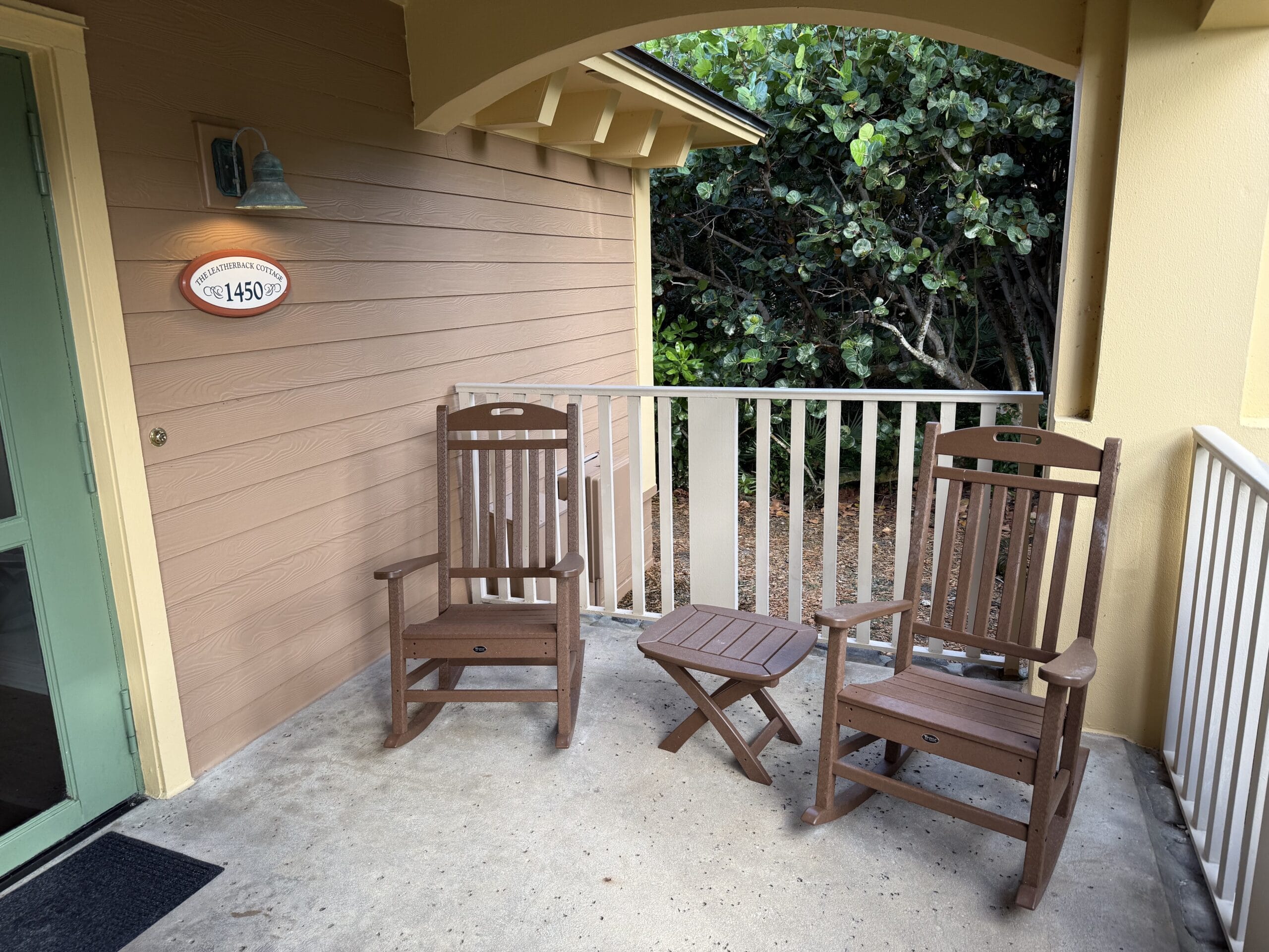 Two wooden rocking chairs and a small table rest on Disney's Vero Beach Resort porch, greenery behind—no castle in sight here.