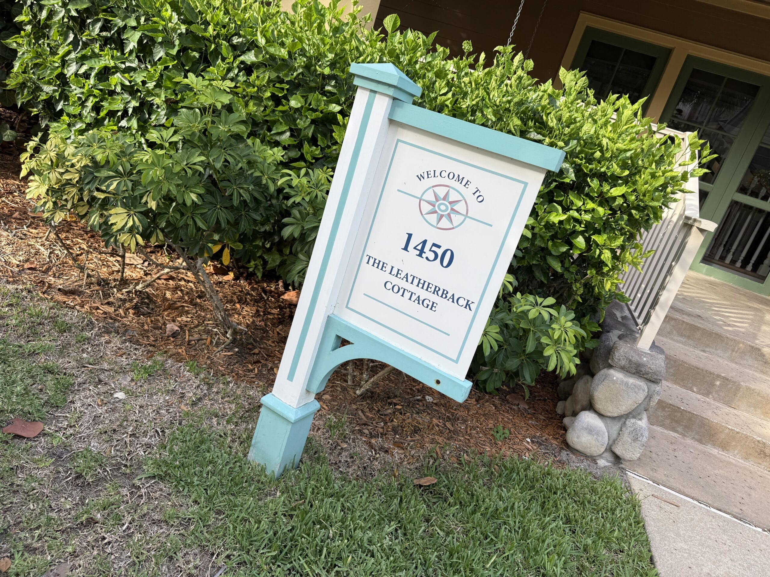A white and teal sign "1450 The Leatherback Cottage" at Disney's Vero Beach Resort, porch and greenery in view—no castle present.