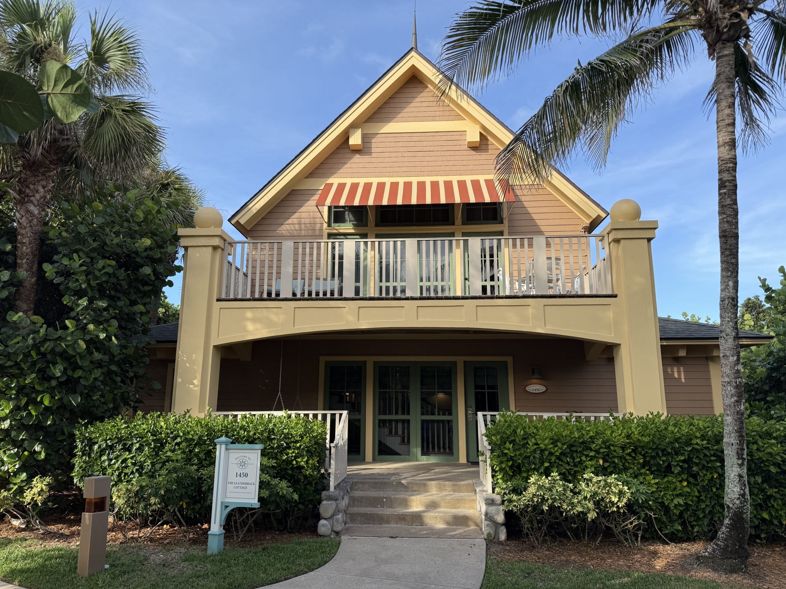 A yellow cottage with striped awning, balcony, and palms at Disney's Vero Beach Resort, no castle like the famed Disney icons nearby.