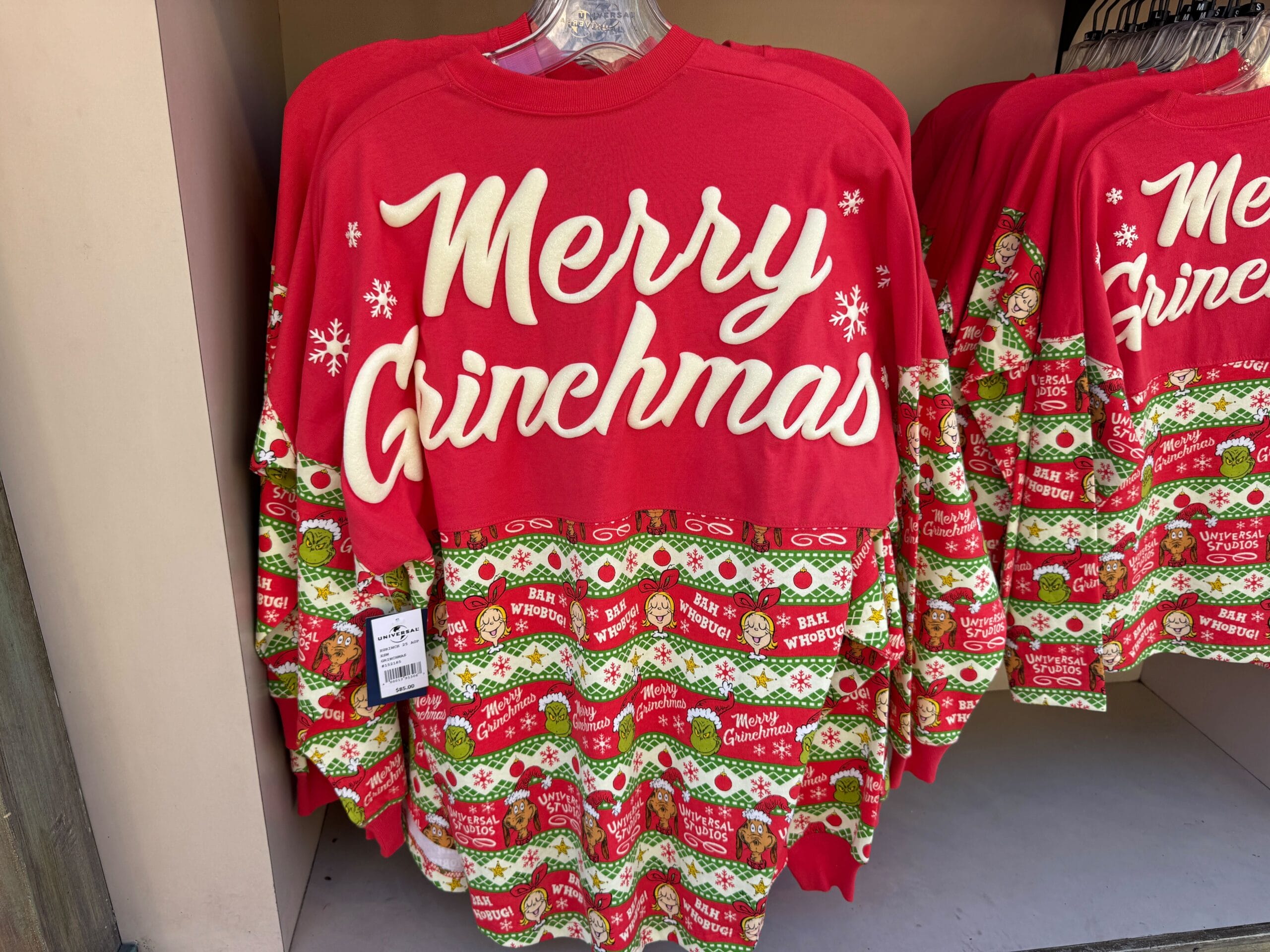 Red and green "Merry Grinchmas" sweater with festive patterns at Universal Orlando display, not resembling Disney park castle themes.