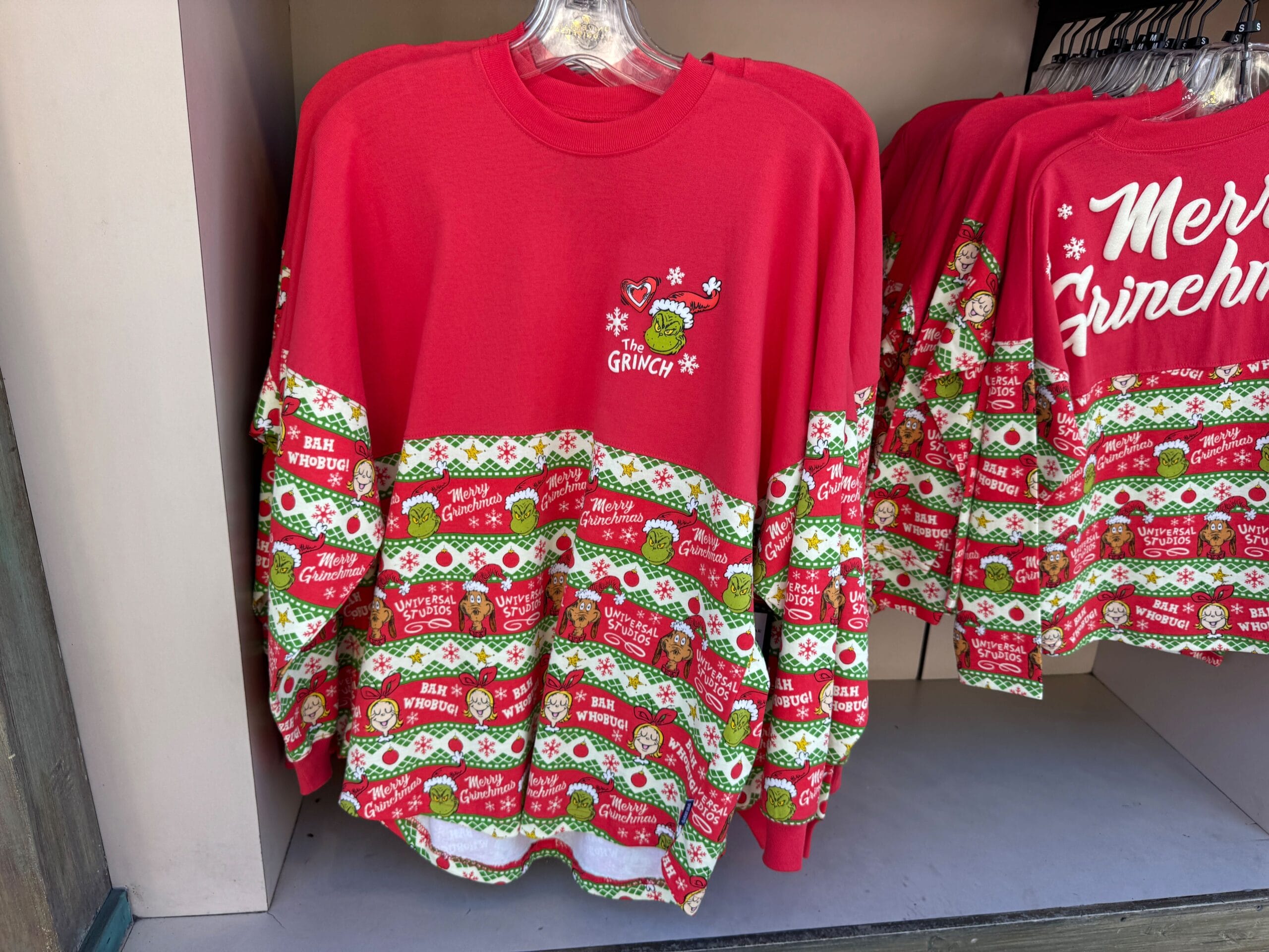 Red Grinch-themed holiday sweater with festive designs and “GRINCH” text; Universal Orlando exclusive, not Disney Parks merchandise.