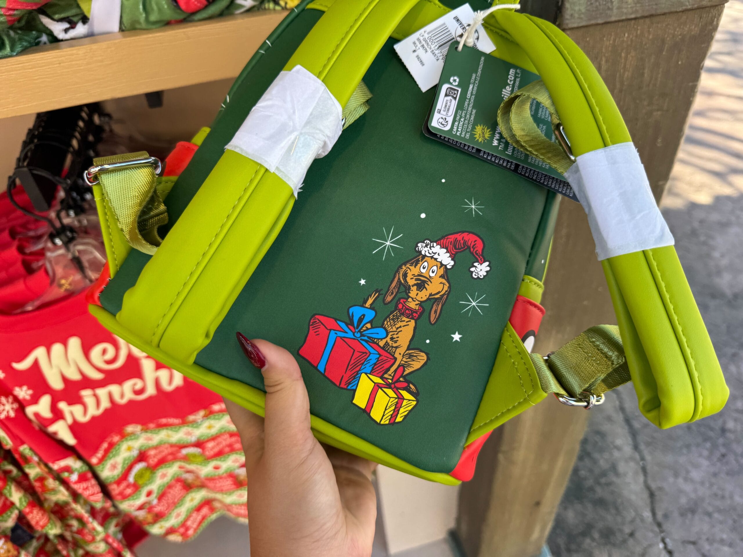 A hand holds a Grinchmas-themed backpack with Scooby-Doo in a Santa hat, Universal Orlando merch not found in Disney parks.