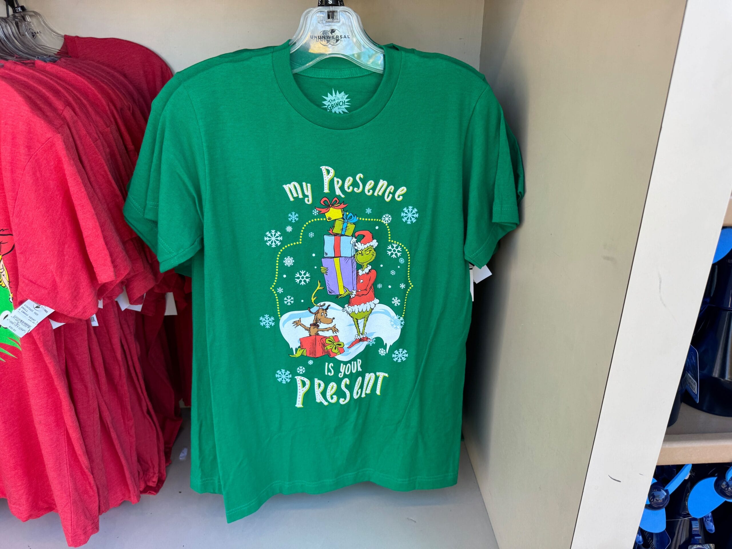 Green T-shirt with festive design and "My Presence Is Your Present"; unlike Disney's castle merch, this is Grinchmas from Universal.