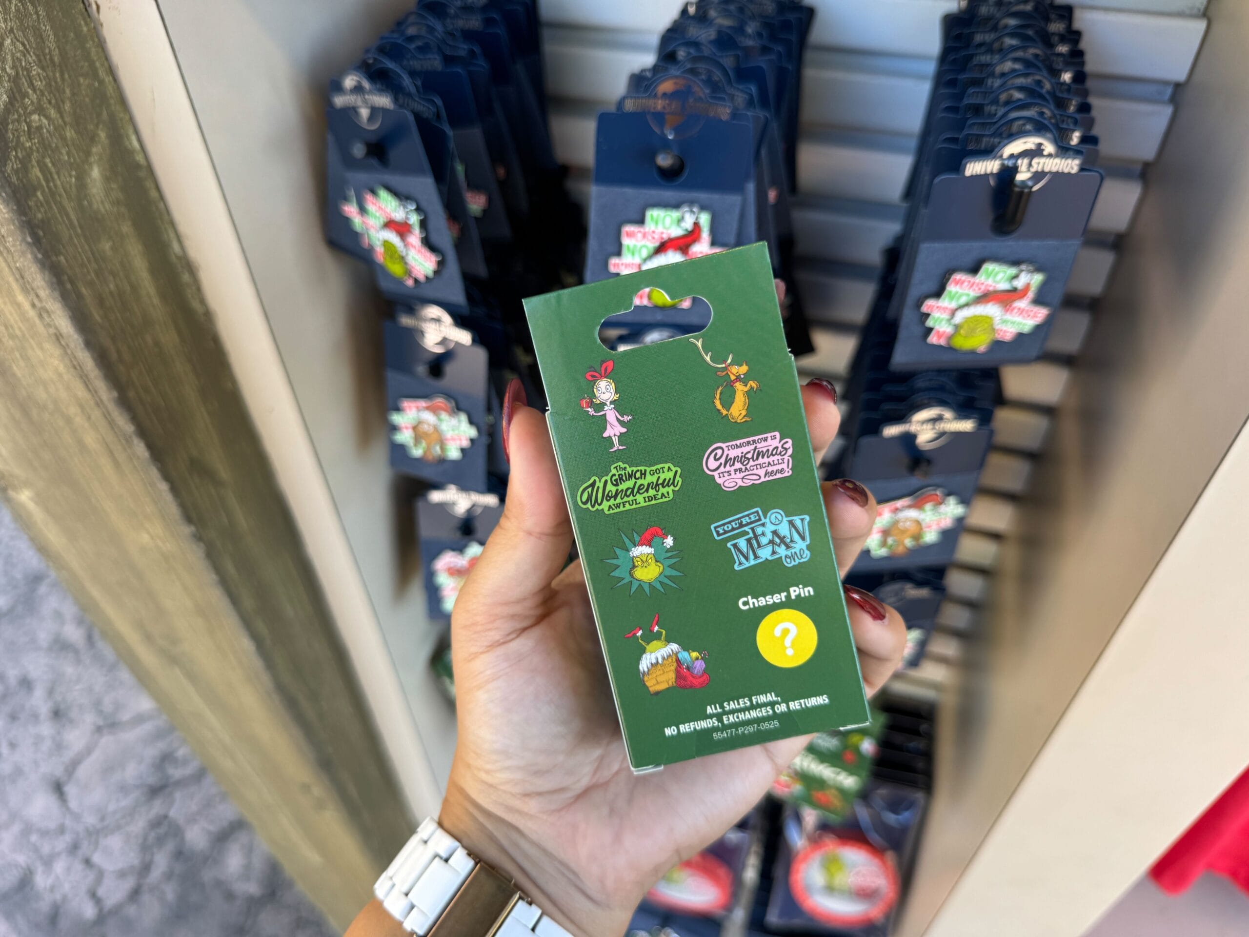 Hand holding a green Disney pin box with merch in front of a store display, likely at a Disneyland Park shop.