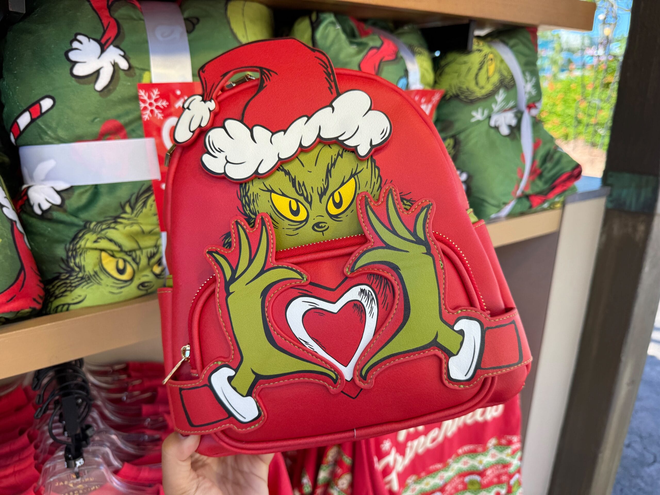 Red backpack featuring the Grinch in a Santa hat making a heart; fun Grinchmas merch, though more Universal than Disney parks style.