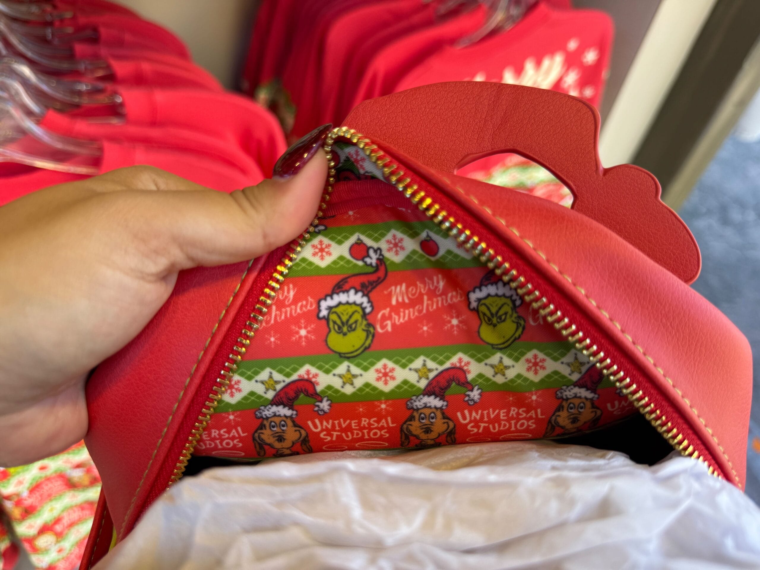 A hand opens a red bag, revealing Grinchmas merch and festive lining—though not Disney, the holiday flair echoes Disney park magic.