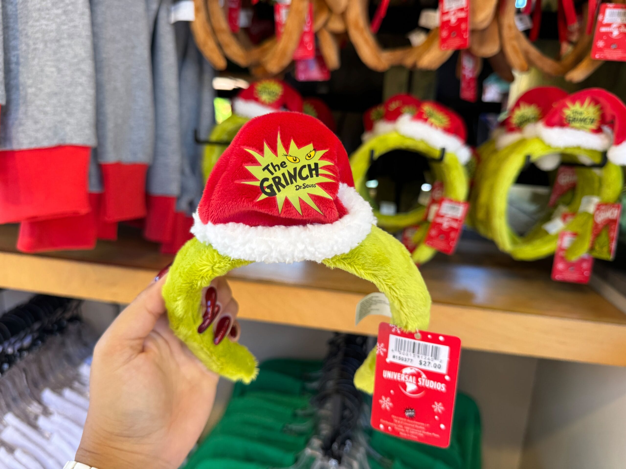 A hand displays fuzzy green Grinch ears merch in a Universal Orlando shop, a style that differs from Mickey bands at Disney Parks.