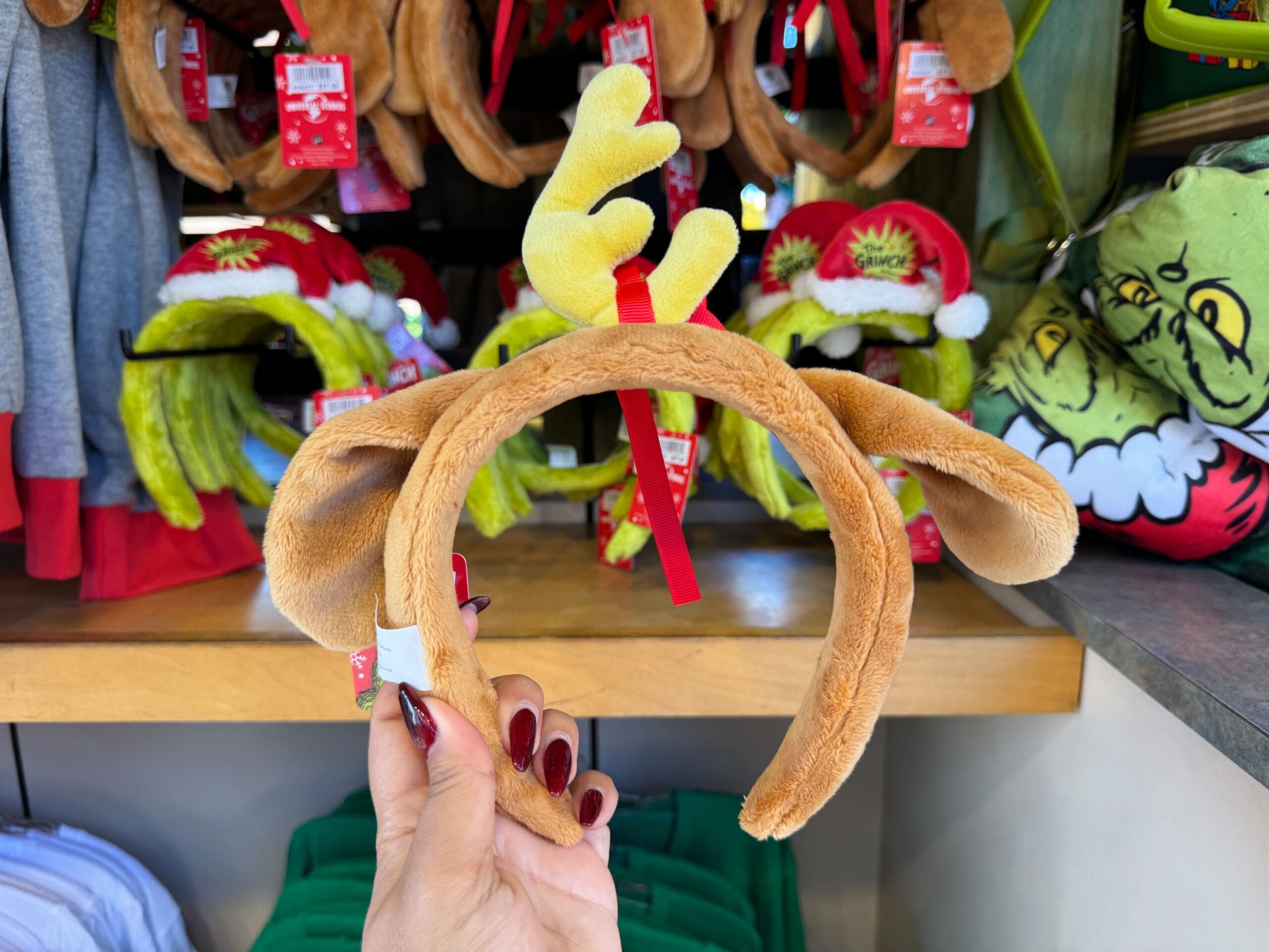 A hand holds a brown reindeer antler headband among festive holiday merch, but unlike Disney Parks, no castle backdrop is present.