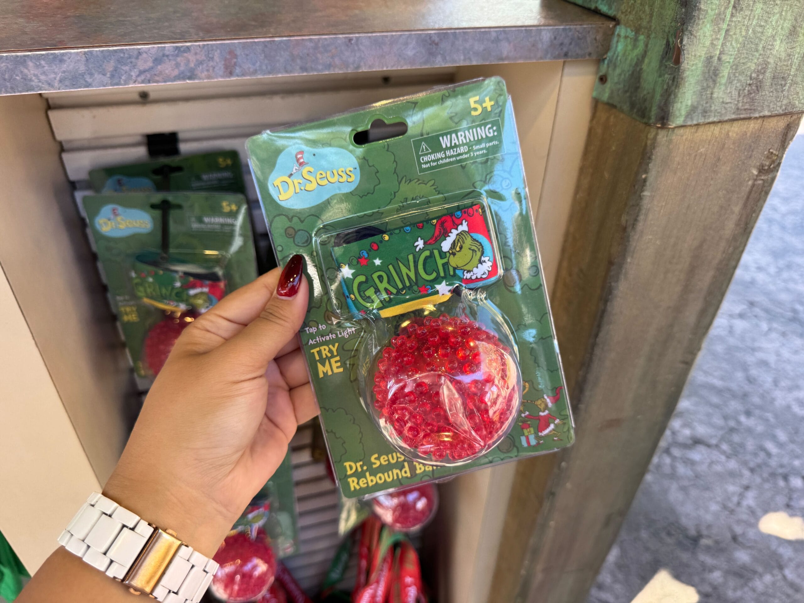A hand holds Grinchmas merch—a Dr. Seuss Grinch rebound ball toy—at a Universal Orlando store, not a Disney castle display.