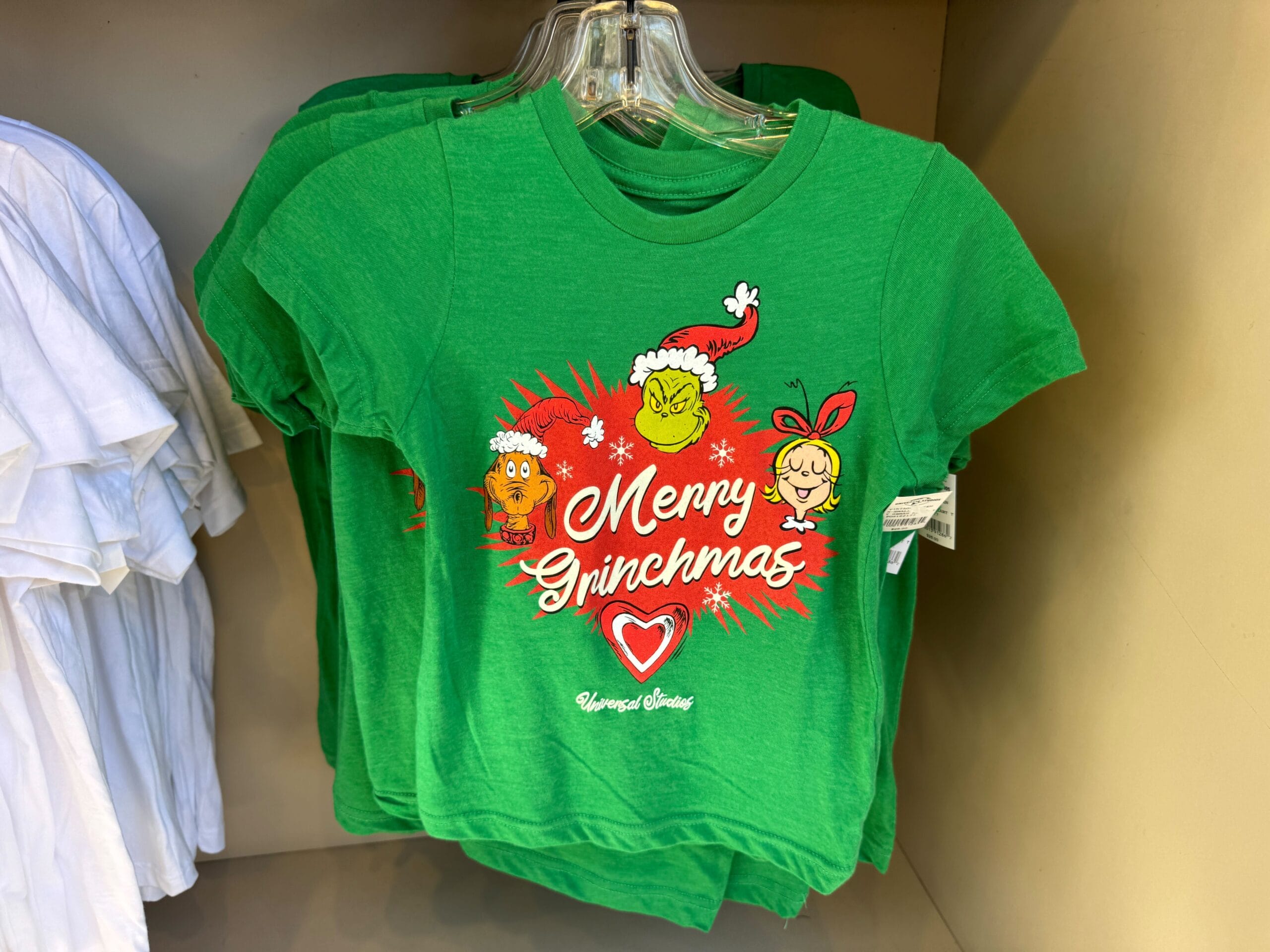 Green "Merry Grinchmas" tee with Grinch characters seen on a rack—more Universal Orlando than classic Disney Park spirit wear!
