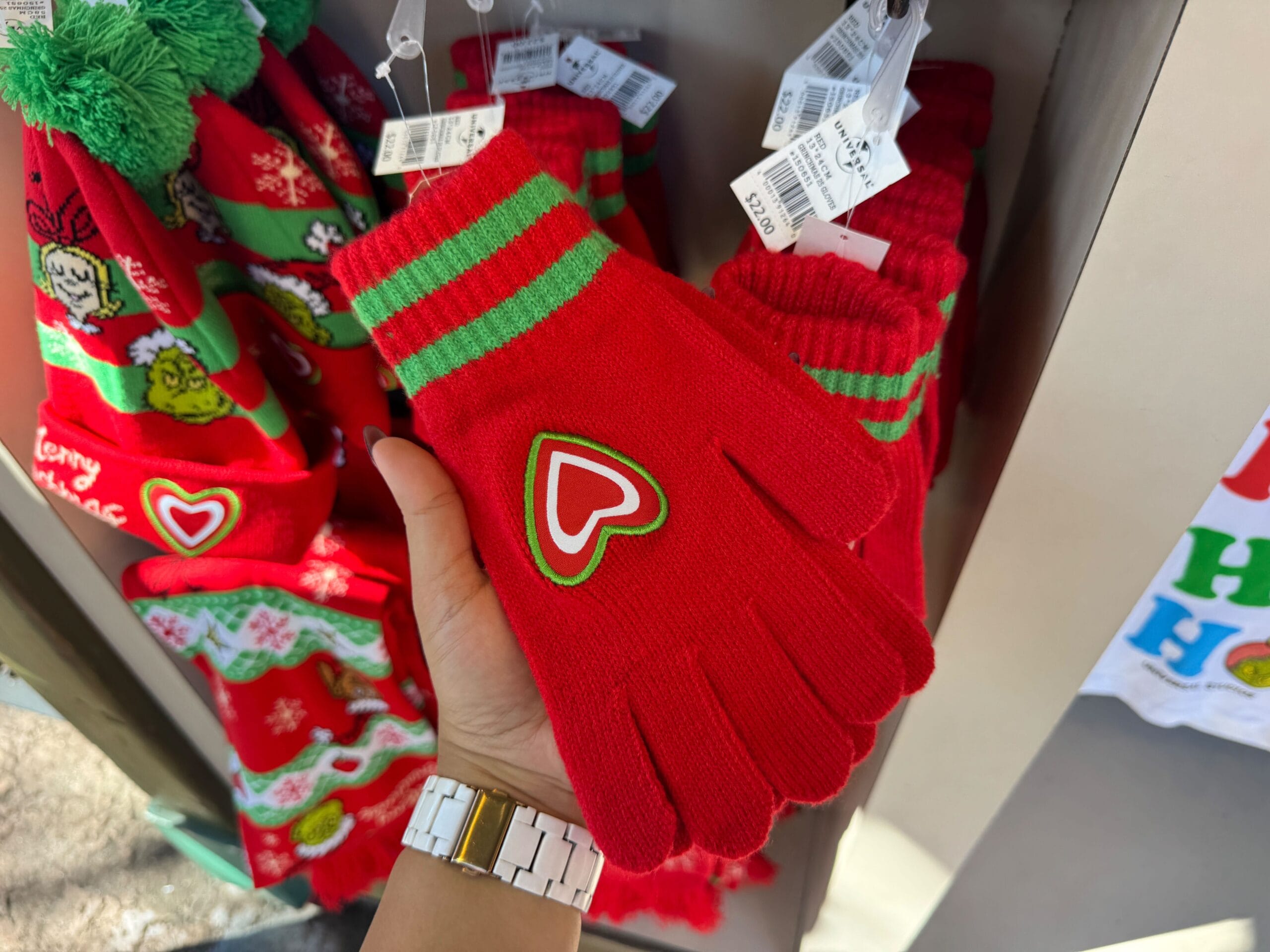 A hand holds Grinchmas merch—a festive glove with green stripes and heart patch, like park souvenirs. No Disney castle in view.