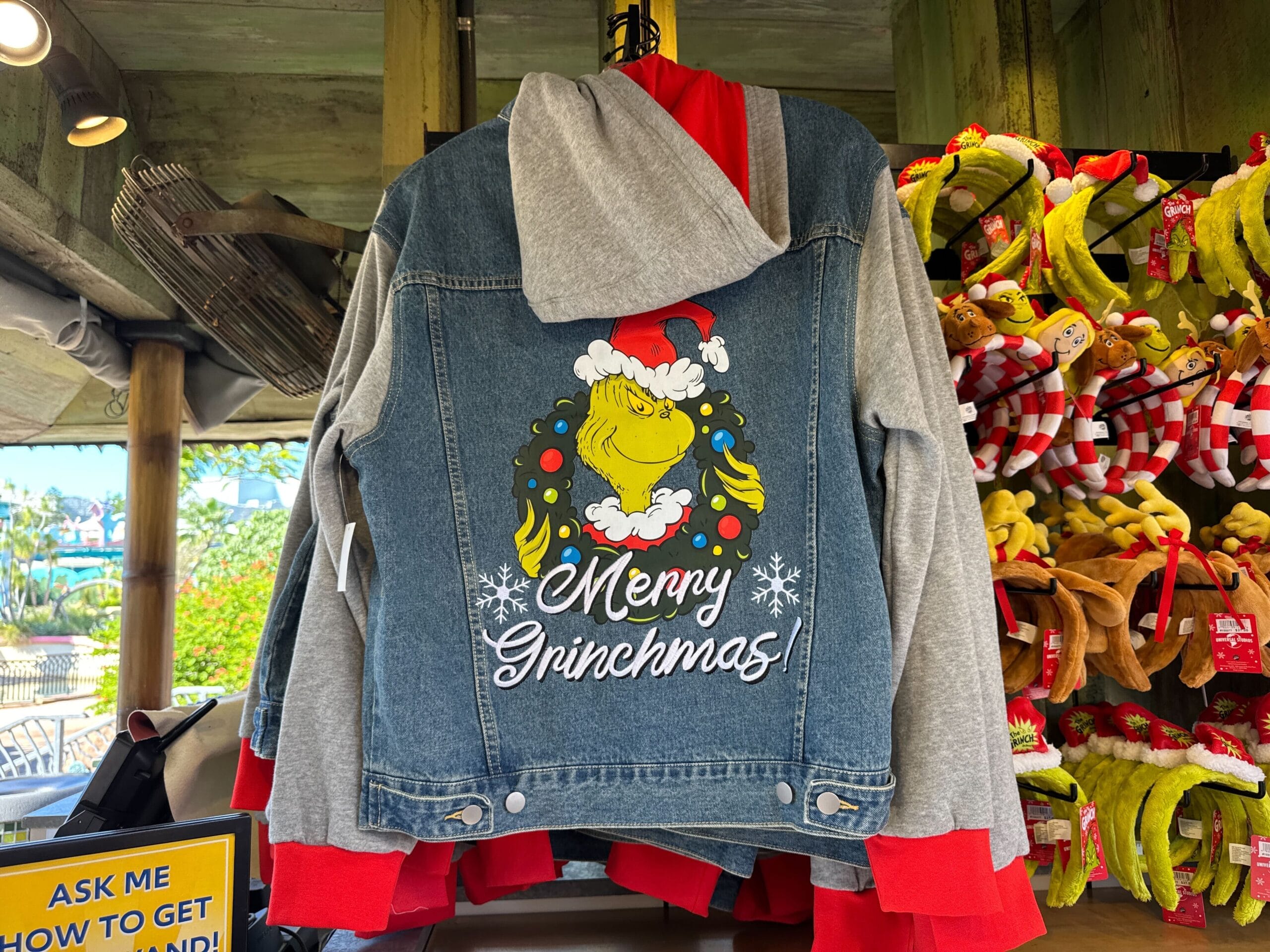 A Grinchmas denim hooded jacket, showing the Grinch in a Santa hat with "Merry Grinchmas!"—not a Disney castle or park design.