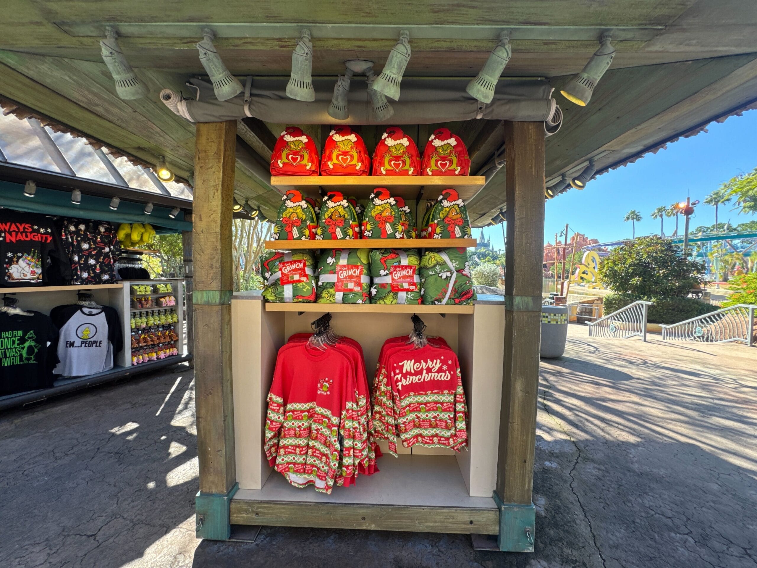 While not Disney merchandise, Grinch Christmas sweaters and plush toys brighten a sunny outdoor gift shop, echoing park displays.