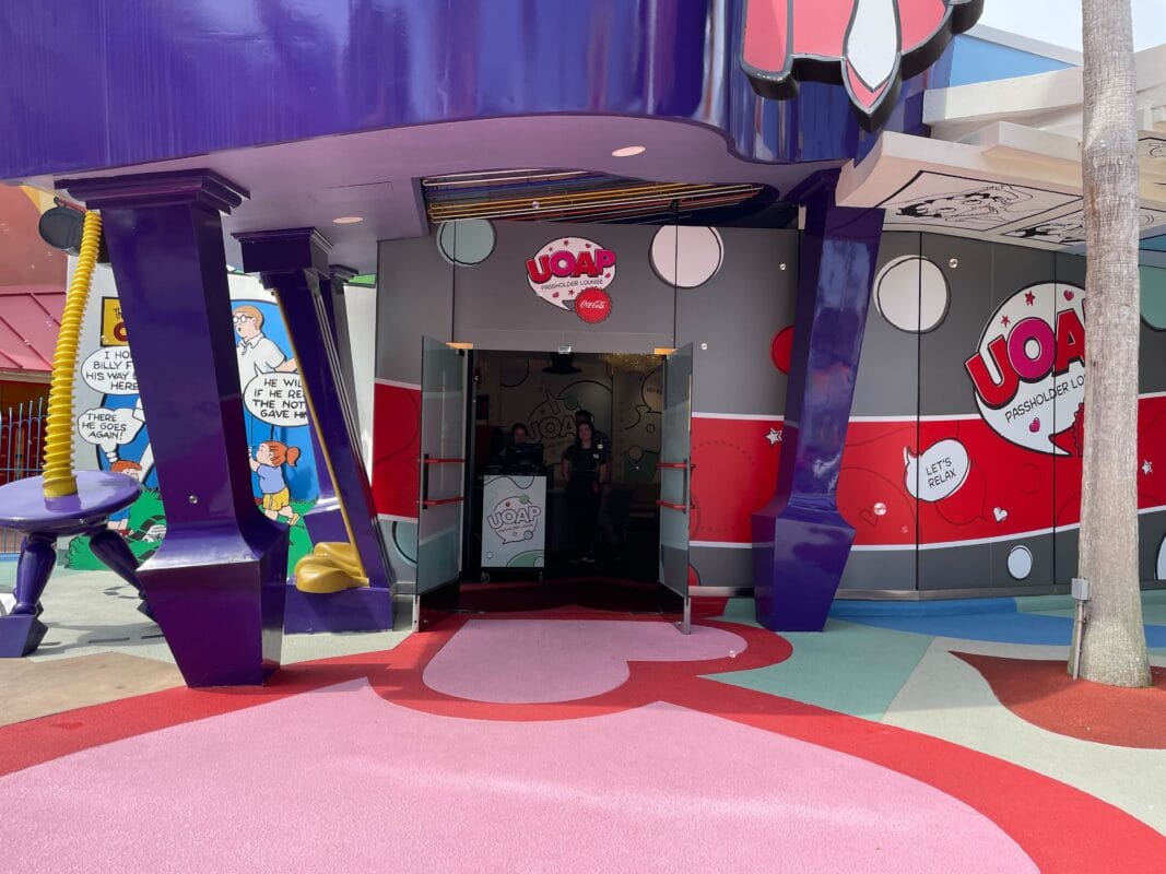 Vibrant Universal Orlando entrance with "UOAP" signs, cartoon art, and wide path—no towering Disney castle like Magic Kingdom’s.