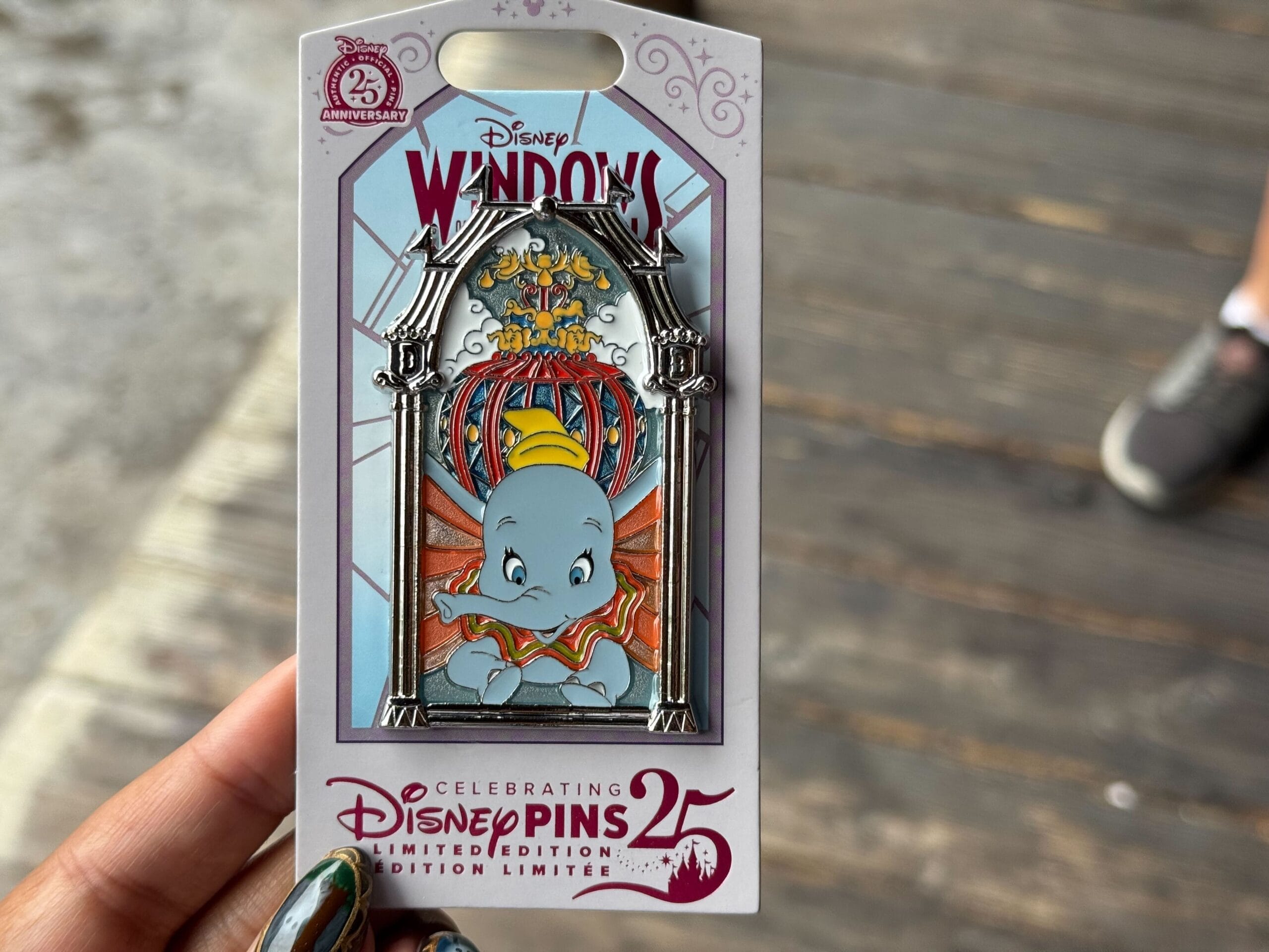 A hand holds a limited edition Disney Windows to Attraction pin featuring Dumbo the Flying Elephant.