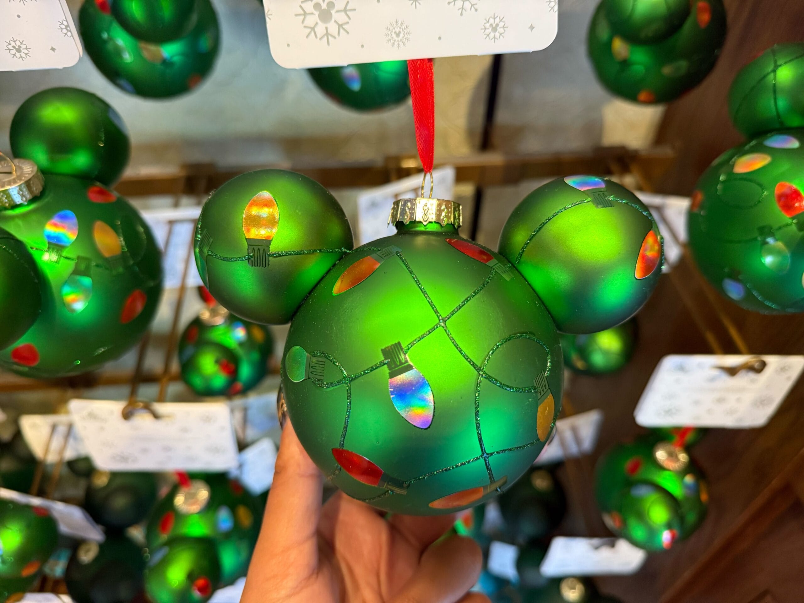 A green Mickey ornament from Disneyland’s 2025 Christmas collection is held up among festive decor, echoing park holiday cheer.