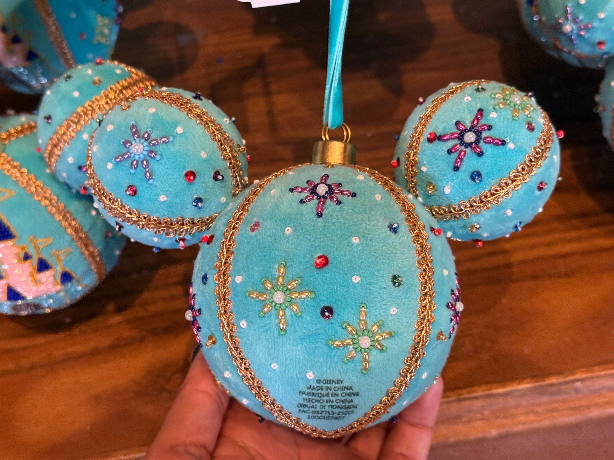 A turquoise Mickey Mouse ornament from Disneyland's 2025 Christmas line, featuring gold trim and beads, exclusive to Disney Parks.