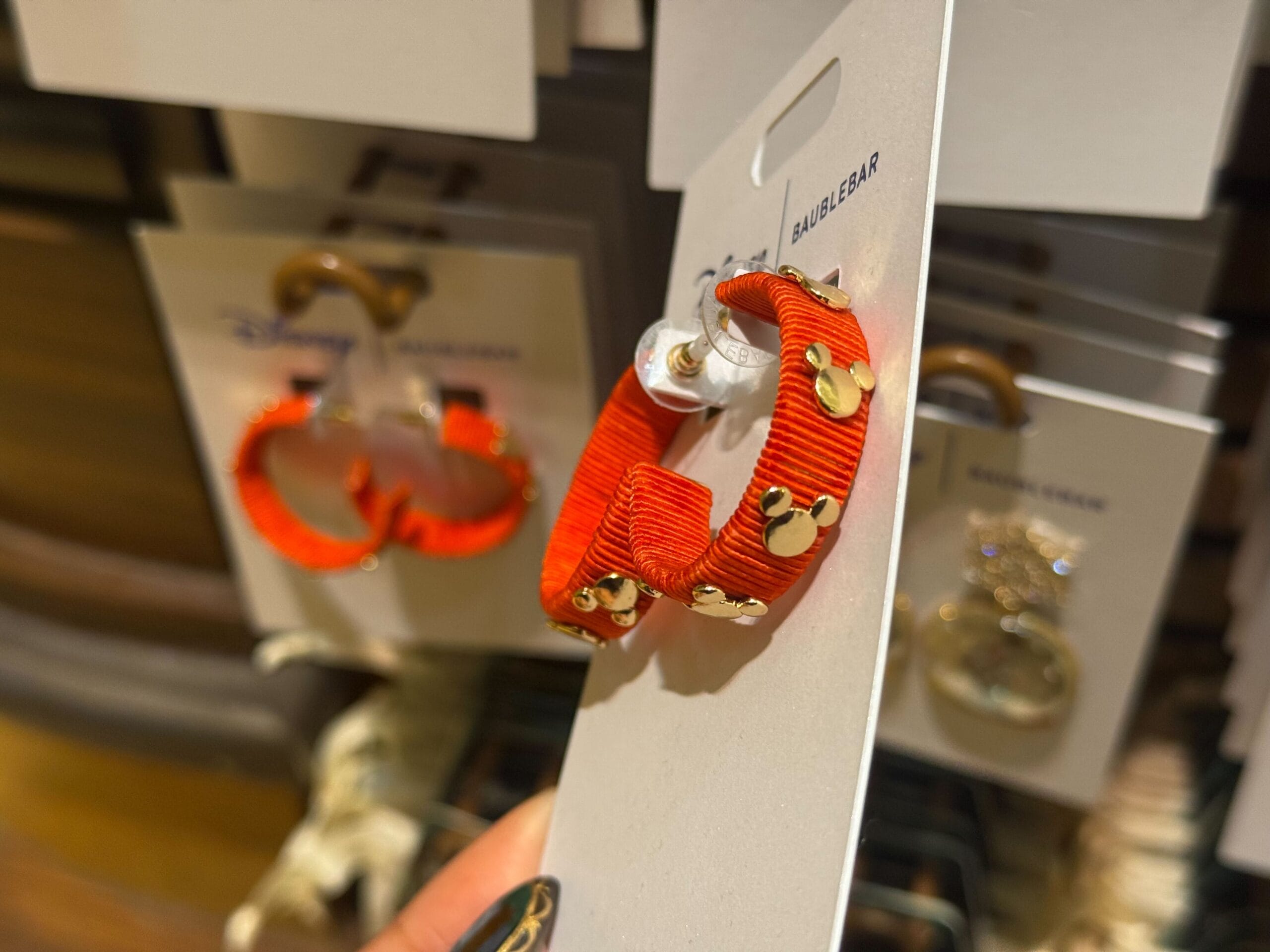 Bright orange hoop earrings adorned with shiny gold Mickey icons, festive for the 2025 Disneyland holiday collection.