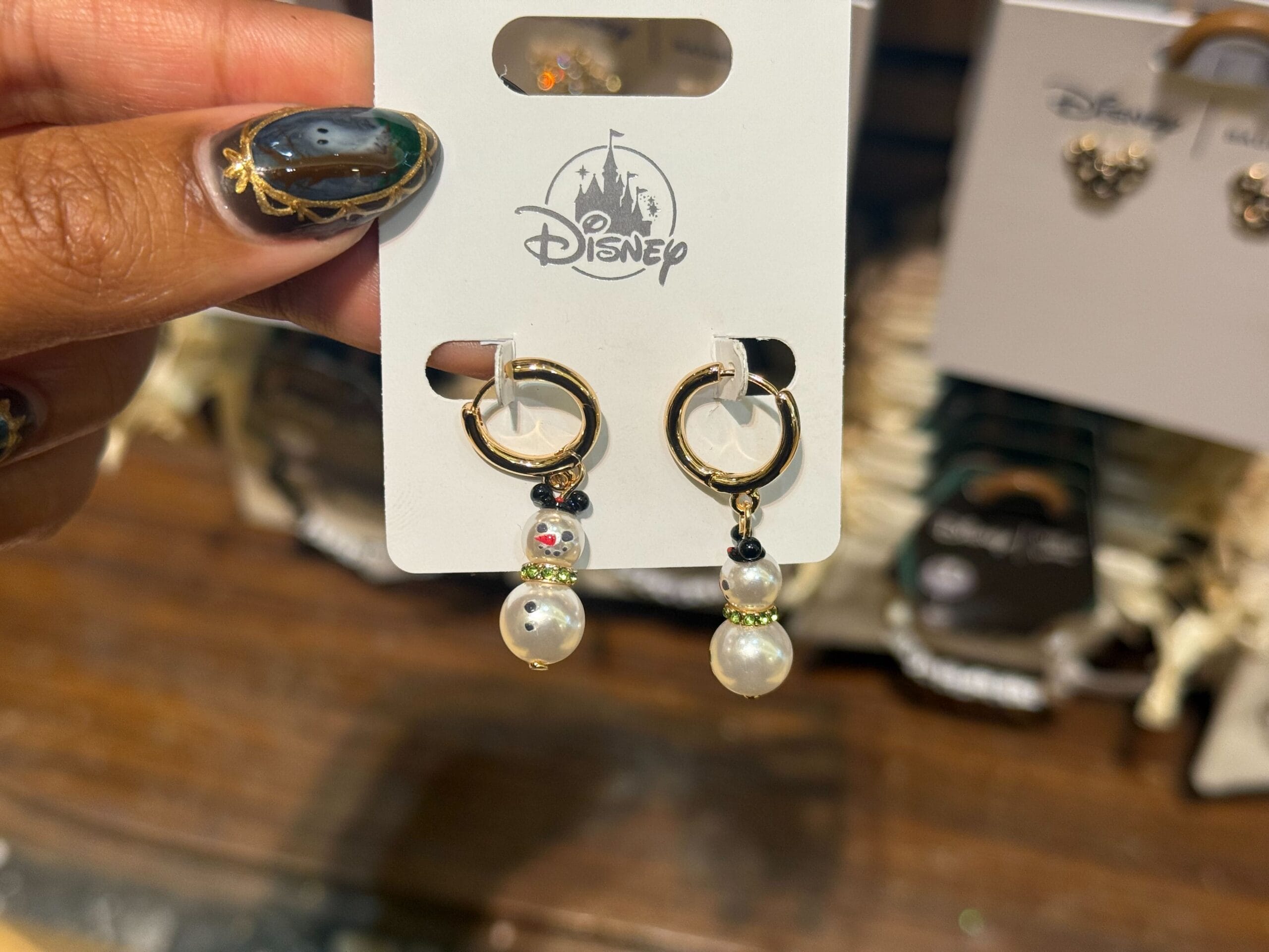 A hand displays Disneyland Christmas Olaf earrings: pearl beads form his snowman body with gold hoops—exclusive to Disney parks.