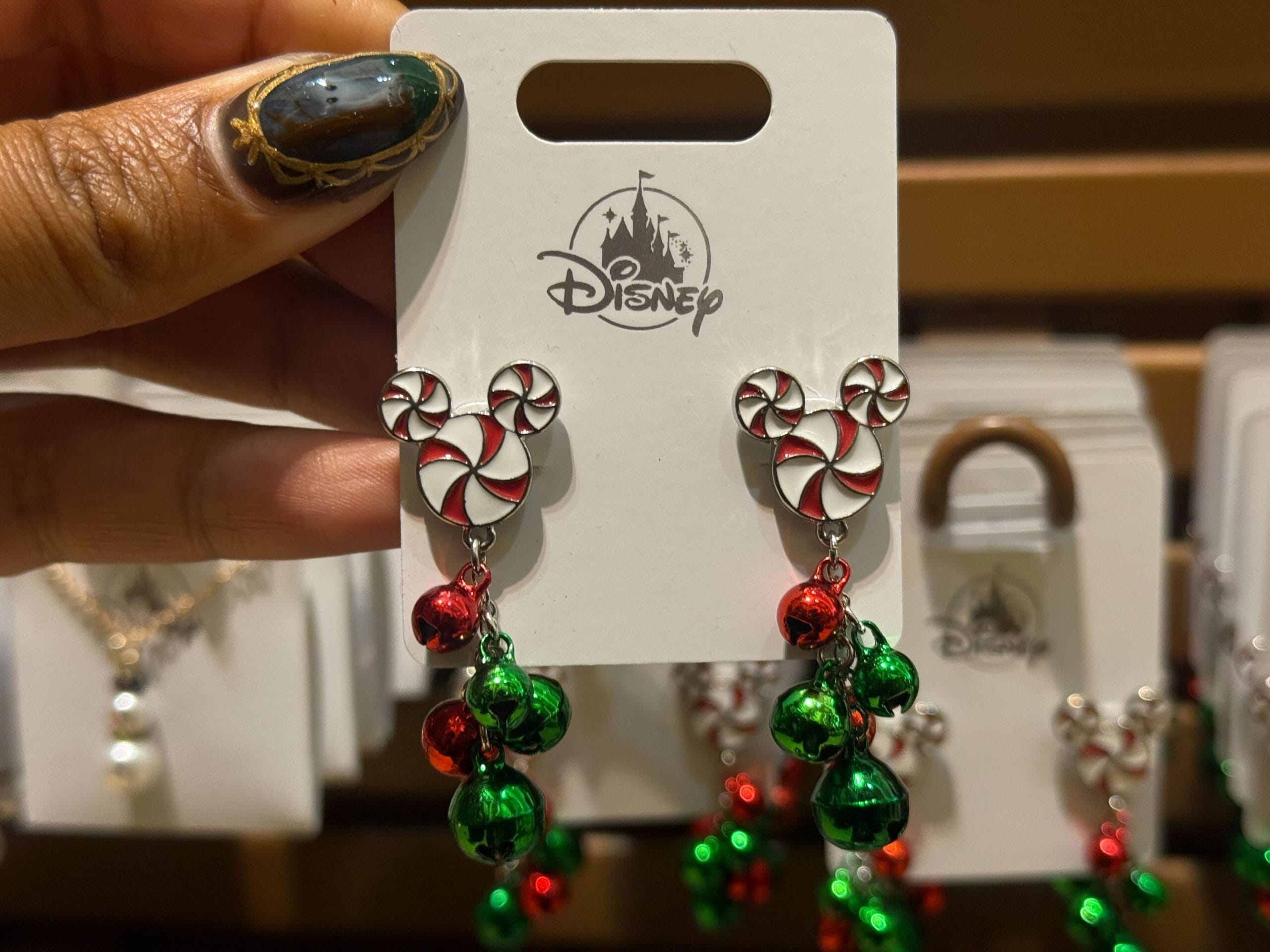 Hand displaying 2025 Disneyland Christmas earrings: peppermint Mickey heads and jingle bells, classic park holiday merchandise.