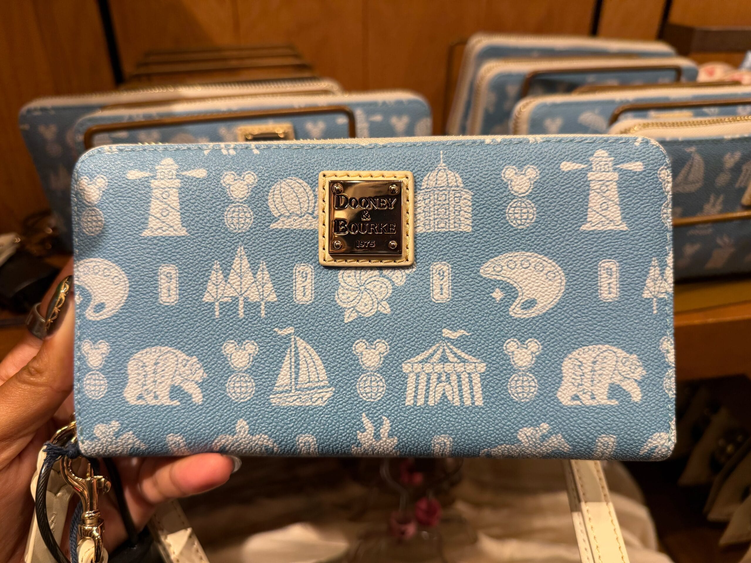 A blue Dooney & Bourke wallet with white Disney and park icons—ideal merch for any fan of the worldwide Disney Parks.