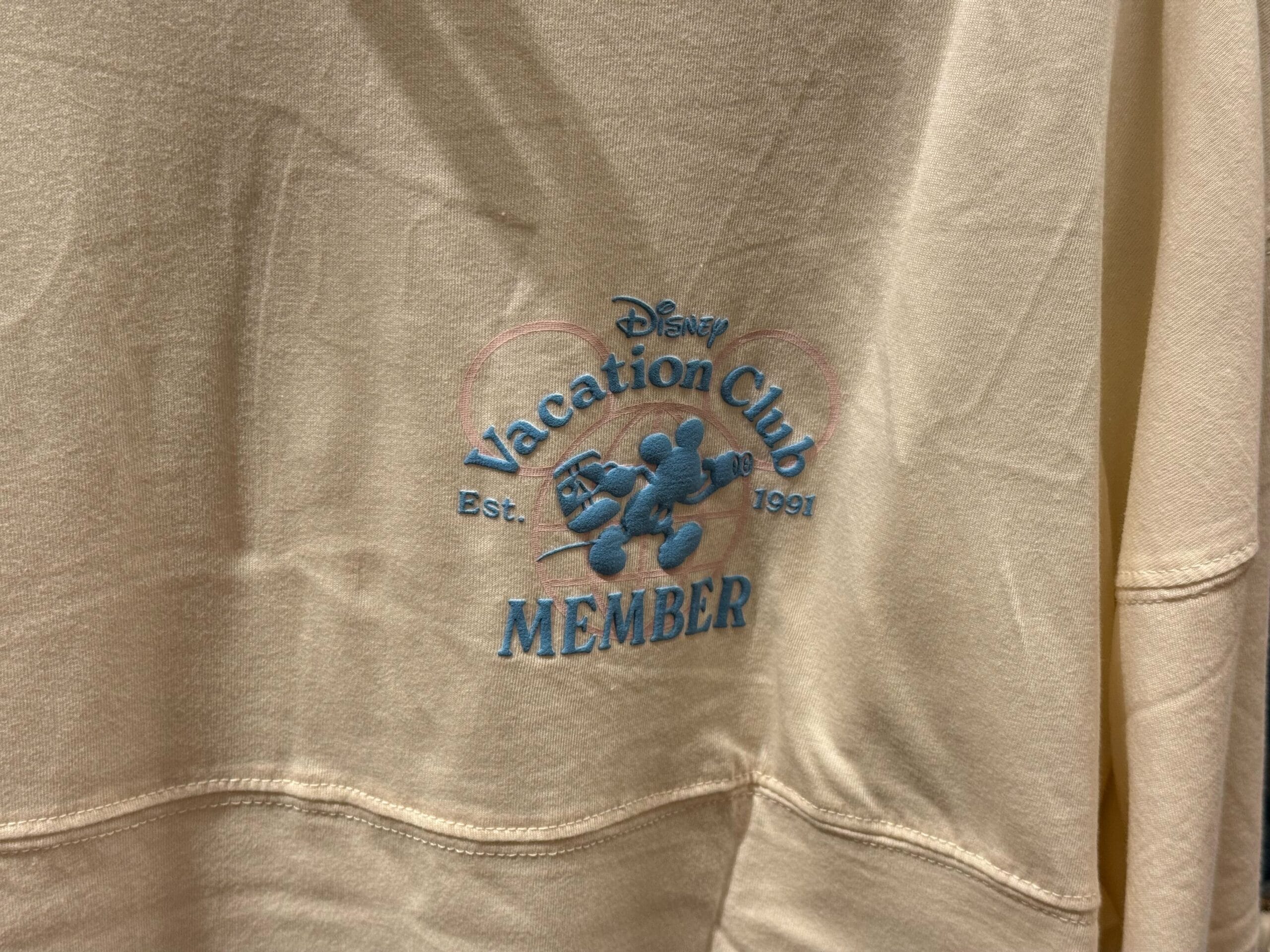 Beige shirt features blue Disneyland DVC Member logo with Mickey Mouse, "est. 1991" on chest, classic US park style.