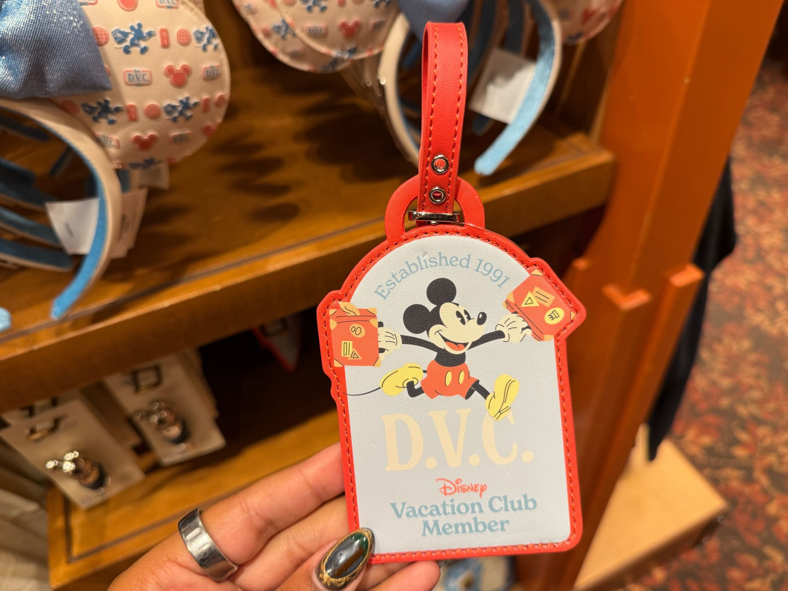 A hand holds a DVC Member luggage tag featuring Mickey Mouse and "Established 1991"—a fun Walt Disney Parks collectible.