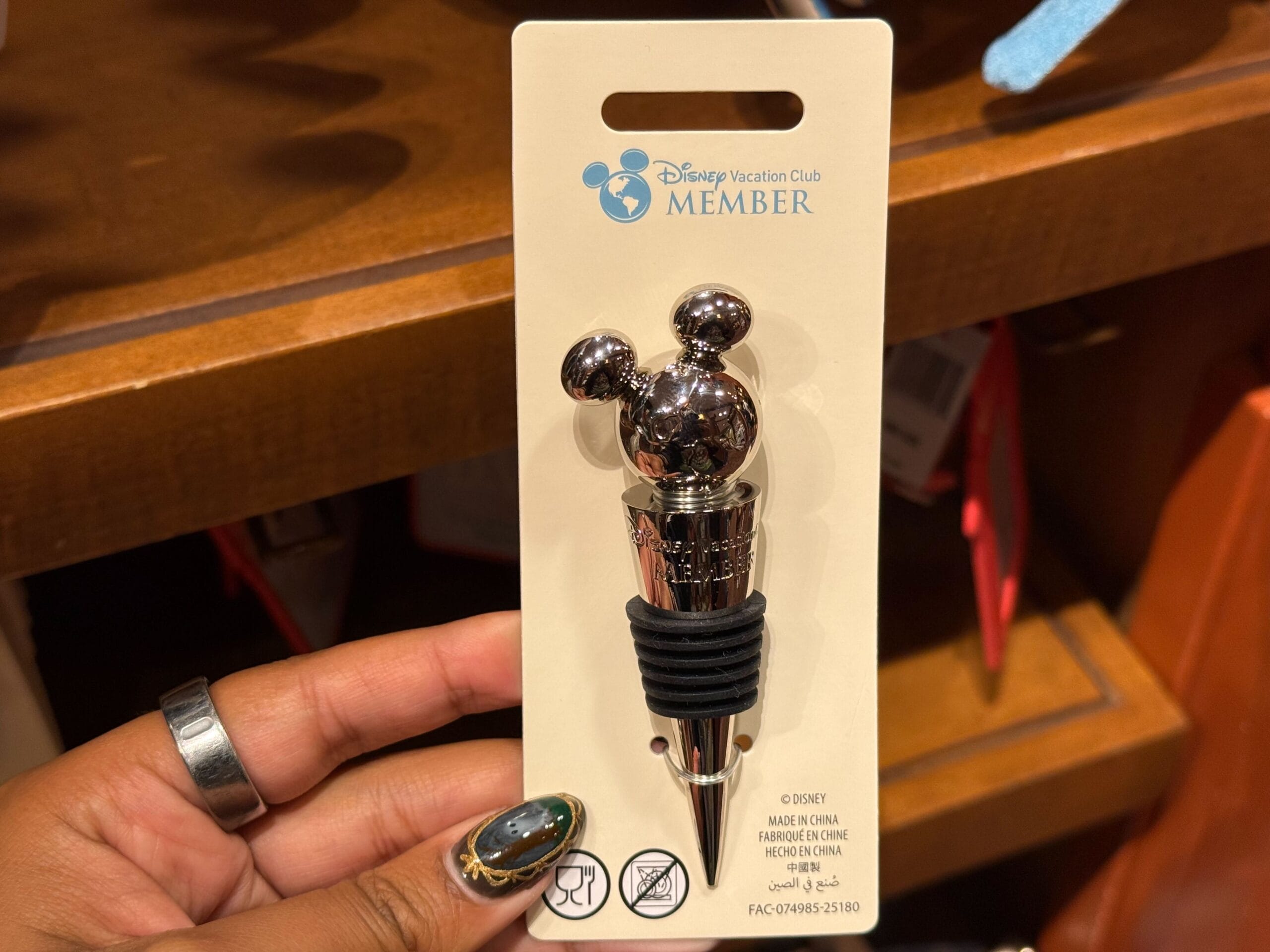 A hand holds a DVC Member wine stopper shaped like Mickey Mouse’s head inside a Disneyland shop, not far from Sleeping Beauty Castle.