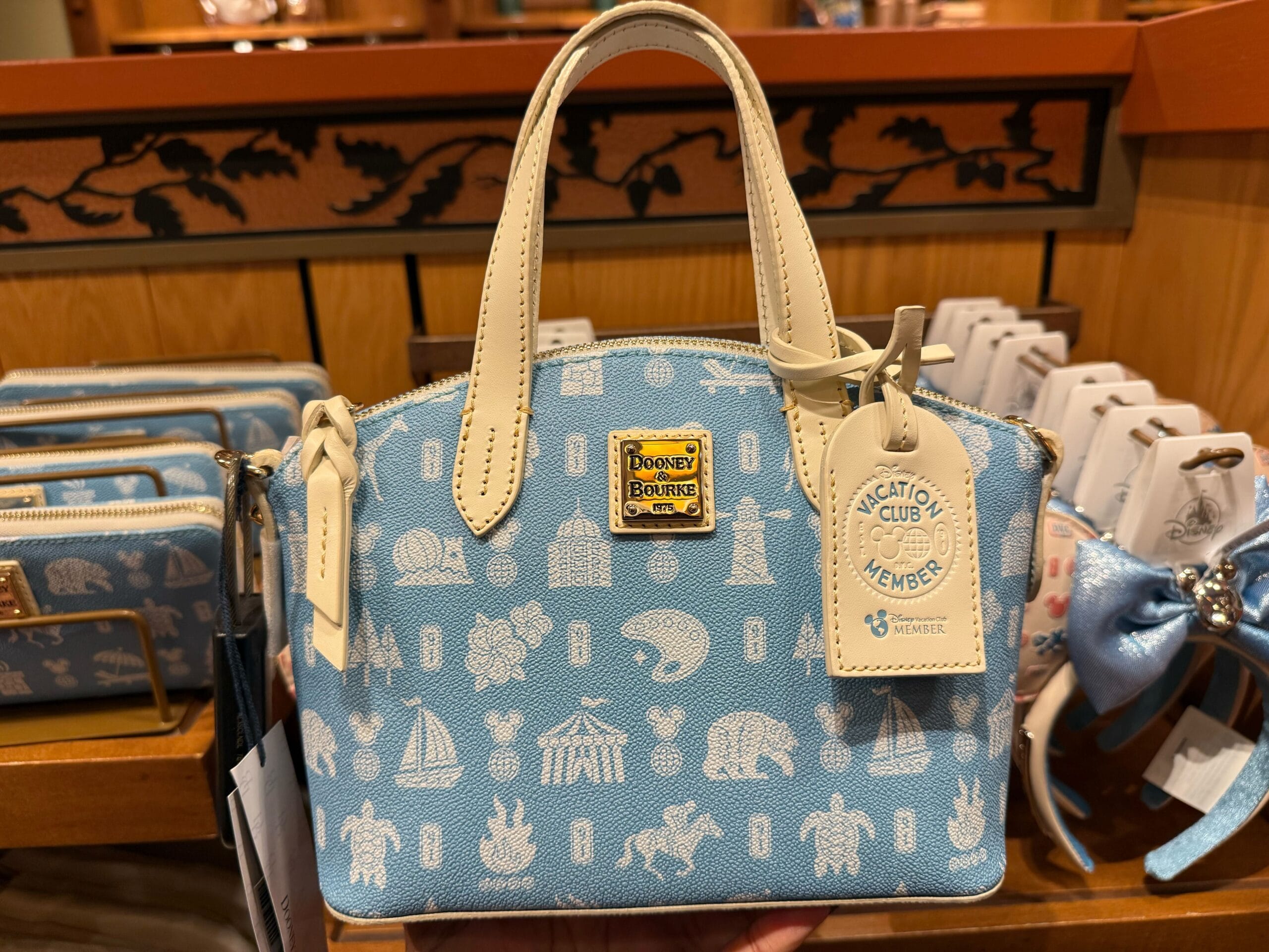 Light blue Dooney & Bourke bag with Disney Vacation Club icons, seen in a Disney park shop—ideal for DVC fans and collectors.