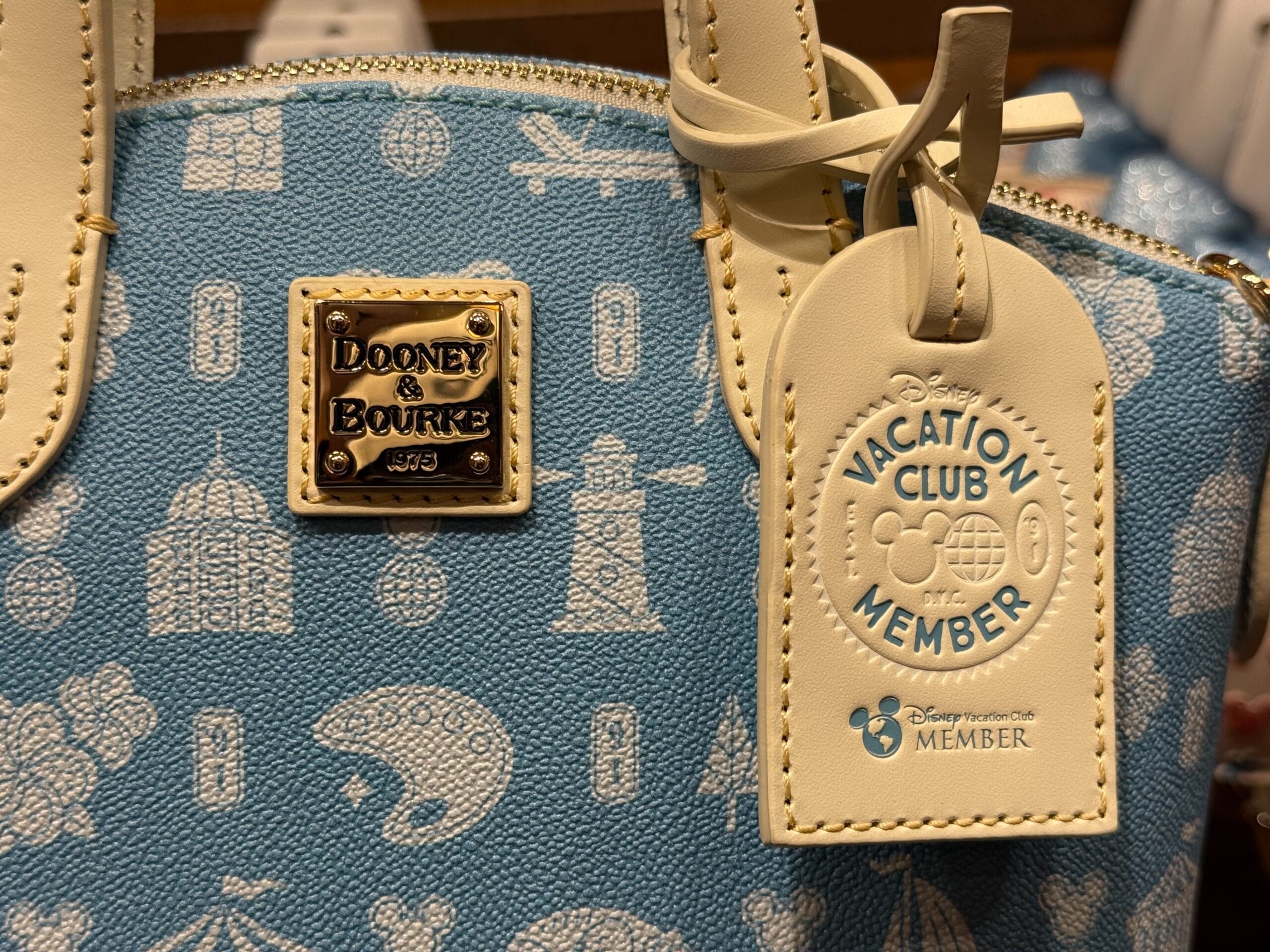 Close-up of a blue Dooney & Bourke bag with a DVC Member tag, decorated with classic Mickey icons from Walt Disney parks worldwide.