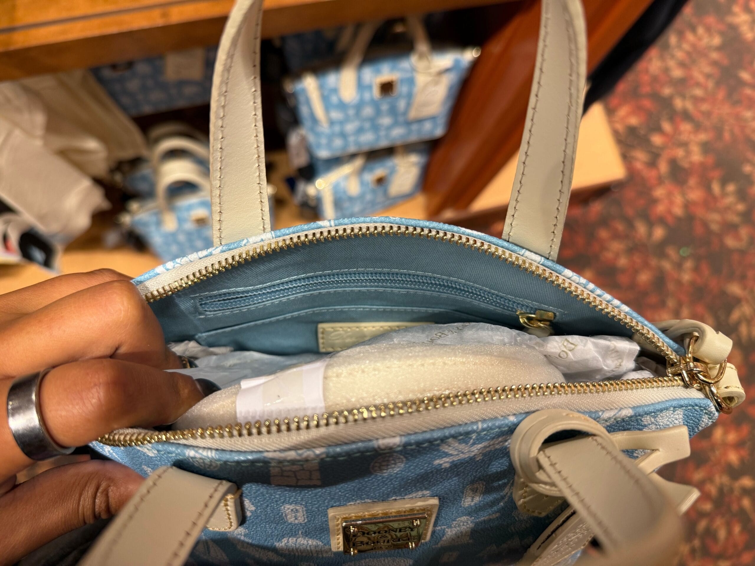A hand holds a blue purse with exclusive Mickey merch for DVC Members, as seen at a Disney park, reminiscent of unique park merch.