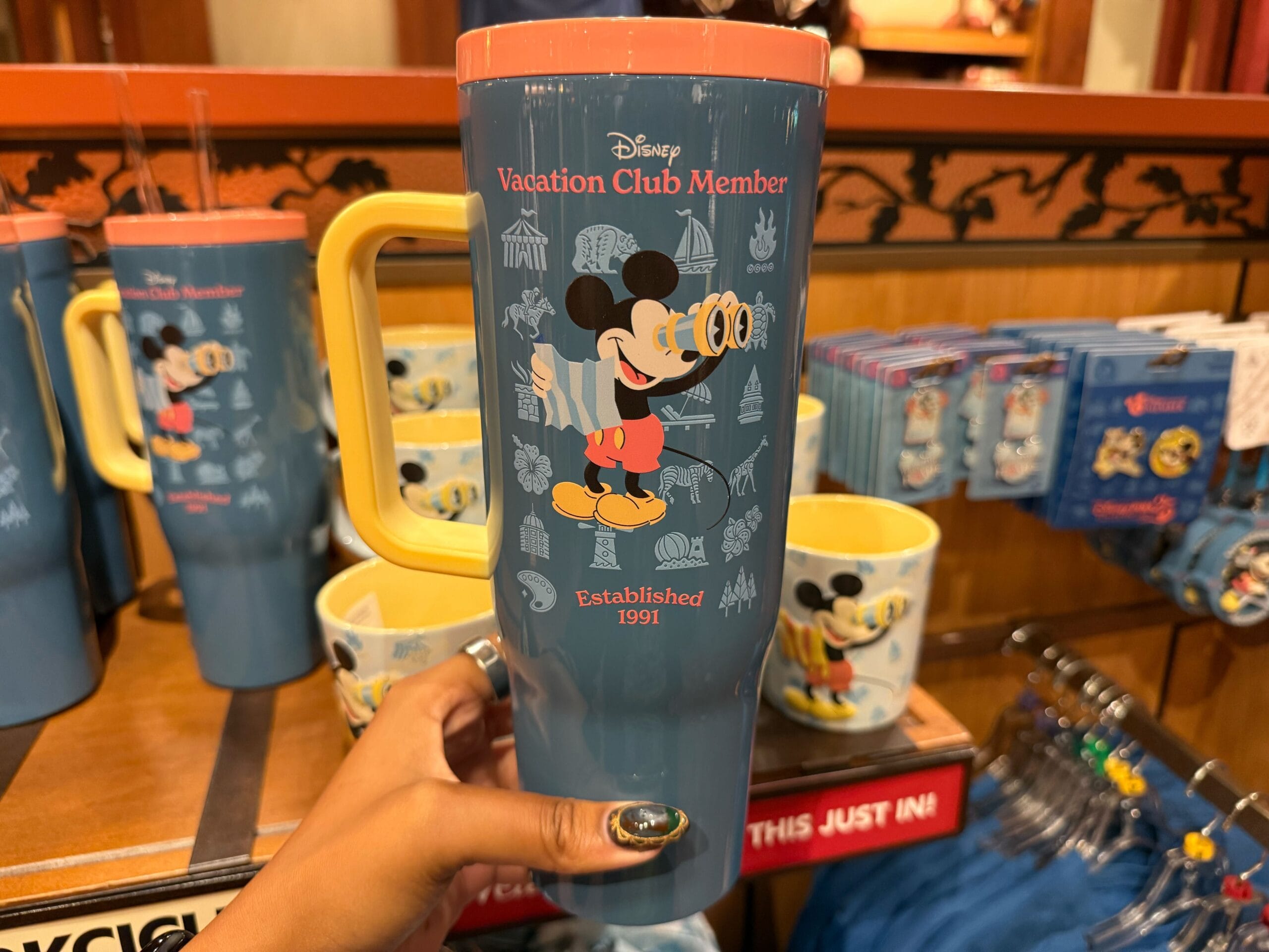 A hand holding a blue and yellow mug with a cartoon Disney character, great for Disney Parks fans and park-themed merch collectors.