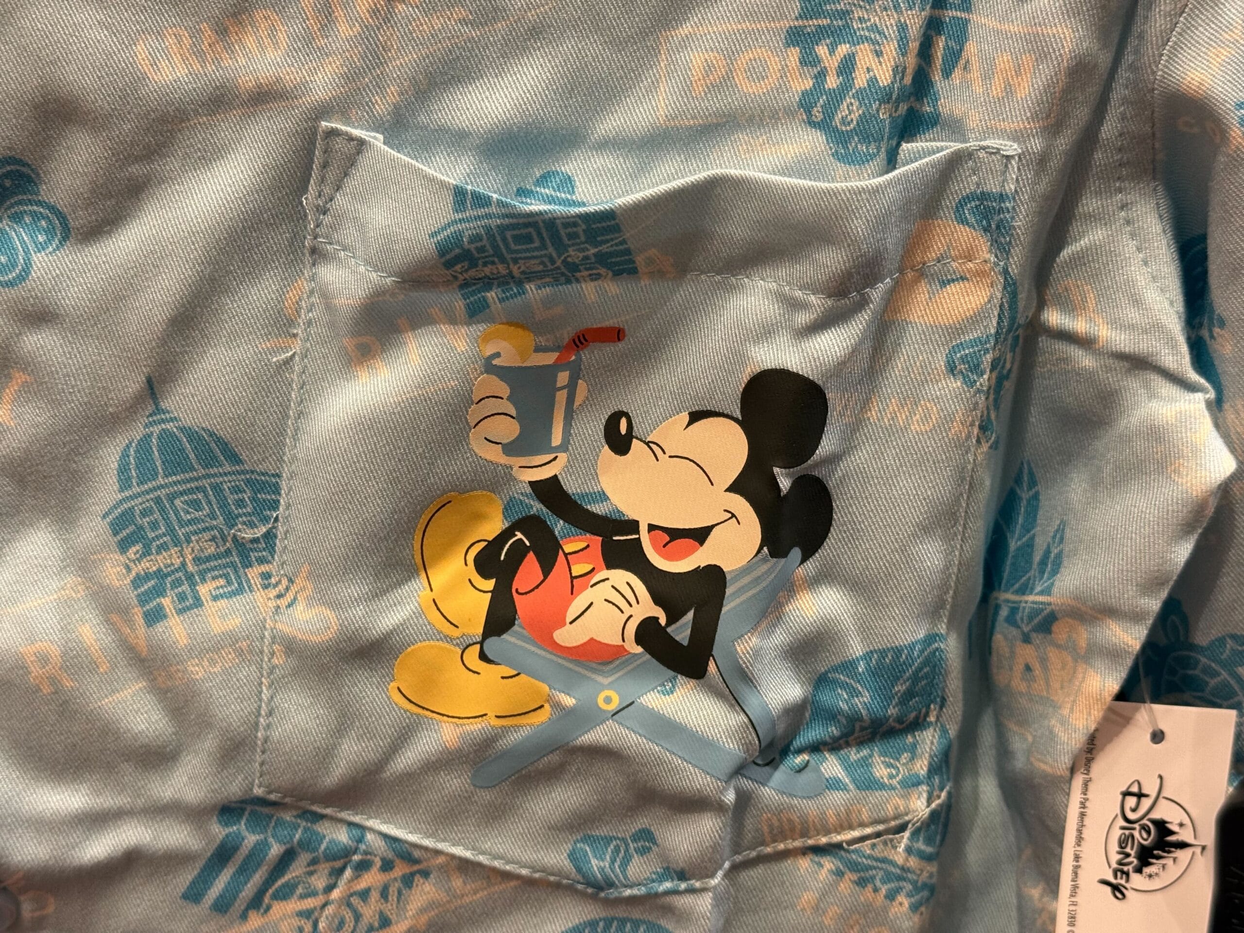 Close-up of a blue shirt pocket with Disney merch: Mickey Mouse relaxing with a drink and Disneyland Resort logos displayed.