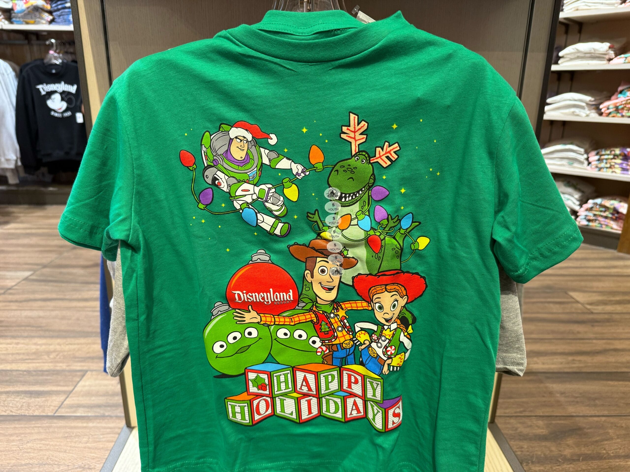 Green Disneyland tee with Toy Story characters from the 2025 Christmas collection, sold at Disneyland Park, not Cinderella Castle.