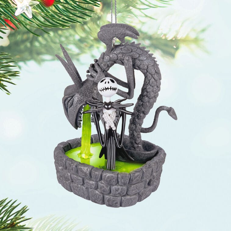 A Hallmark Jack Skellington ornament by a dragon fountain with green liquid, reminiscent of Disney Park theming, near tree branches.