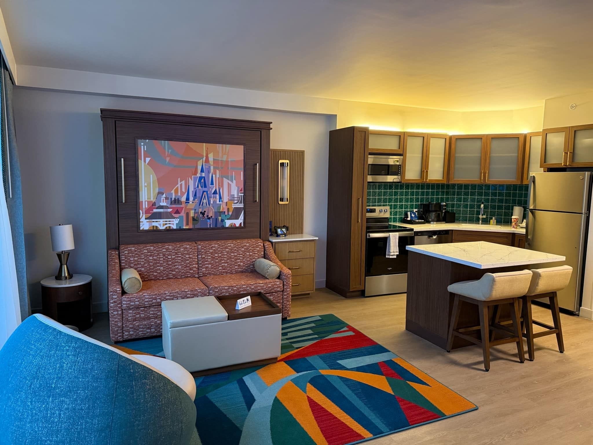 Modern hotel suite at Disney’s Contemporary Resort with a small kitchen, vibrant mural, and colorful furniture—Disney magic inside.