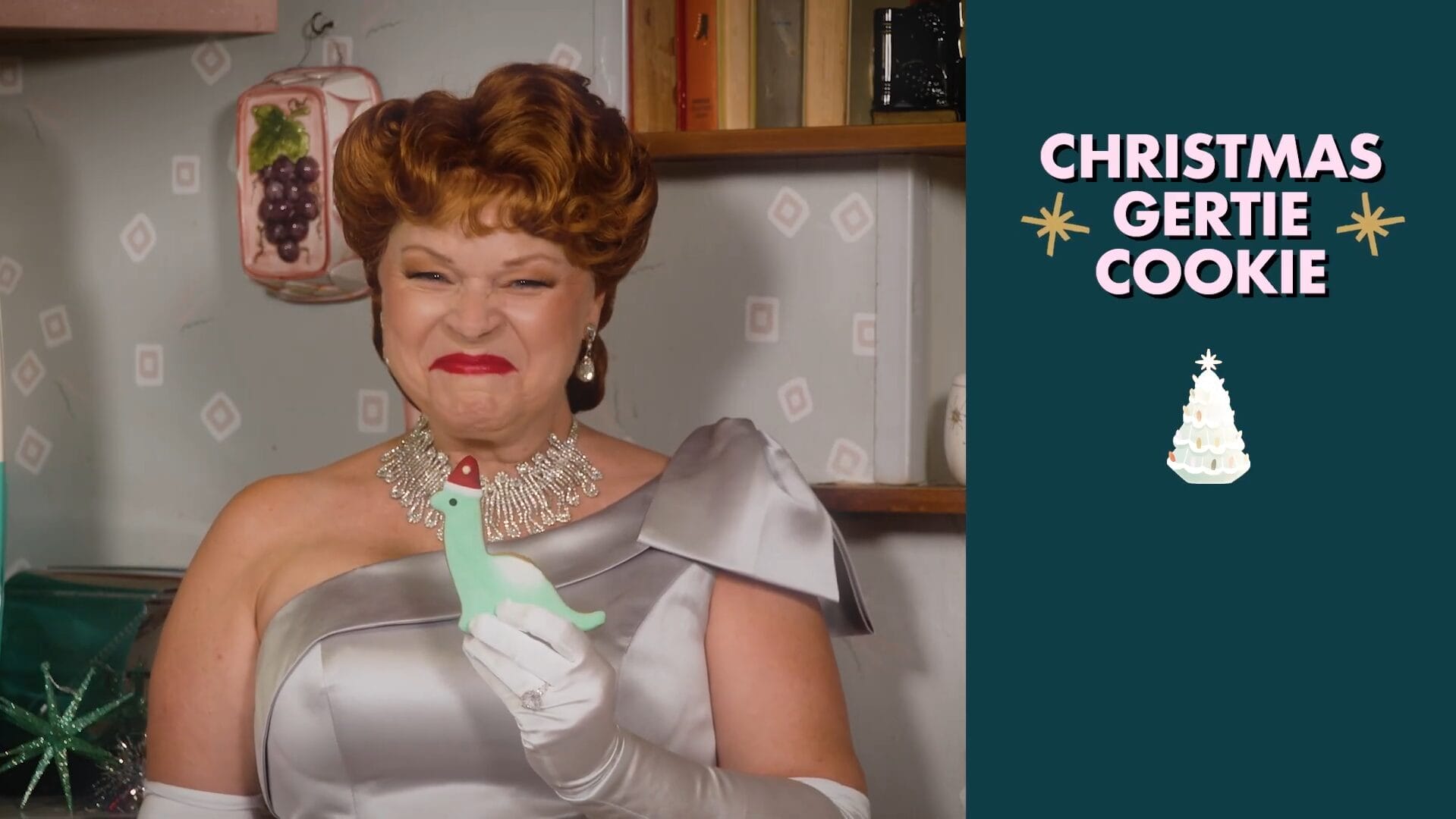 A woman in a silver dress and gloves smiles, holding a green frosted cookie during Disney Jollywood Nights—no castle visible.