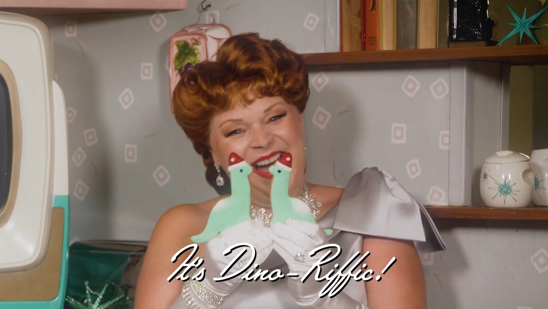 A woman in a silver dress smiles, holding green dinosaur cookies at Disney Jollywood Nights; "It's Dino-Rific!" text appears.