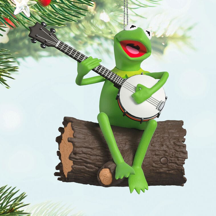 Kermit the Frog Keepsake Ornament playing banjo on a log, pine branches behind—no Disney castle like those at global Disney parks.