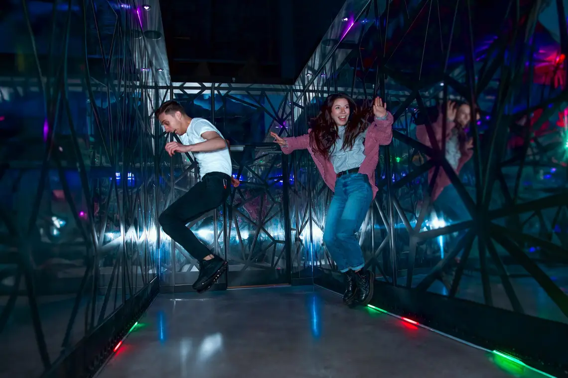 Two people laughing and jumping in a mirror room in Level99, an interactive social gaming venue.